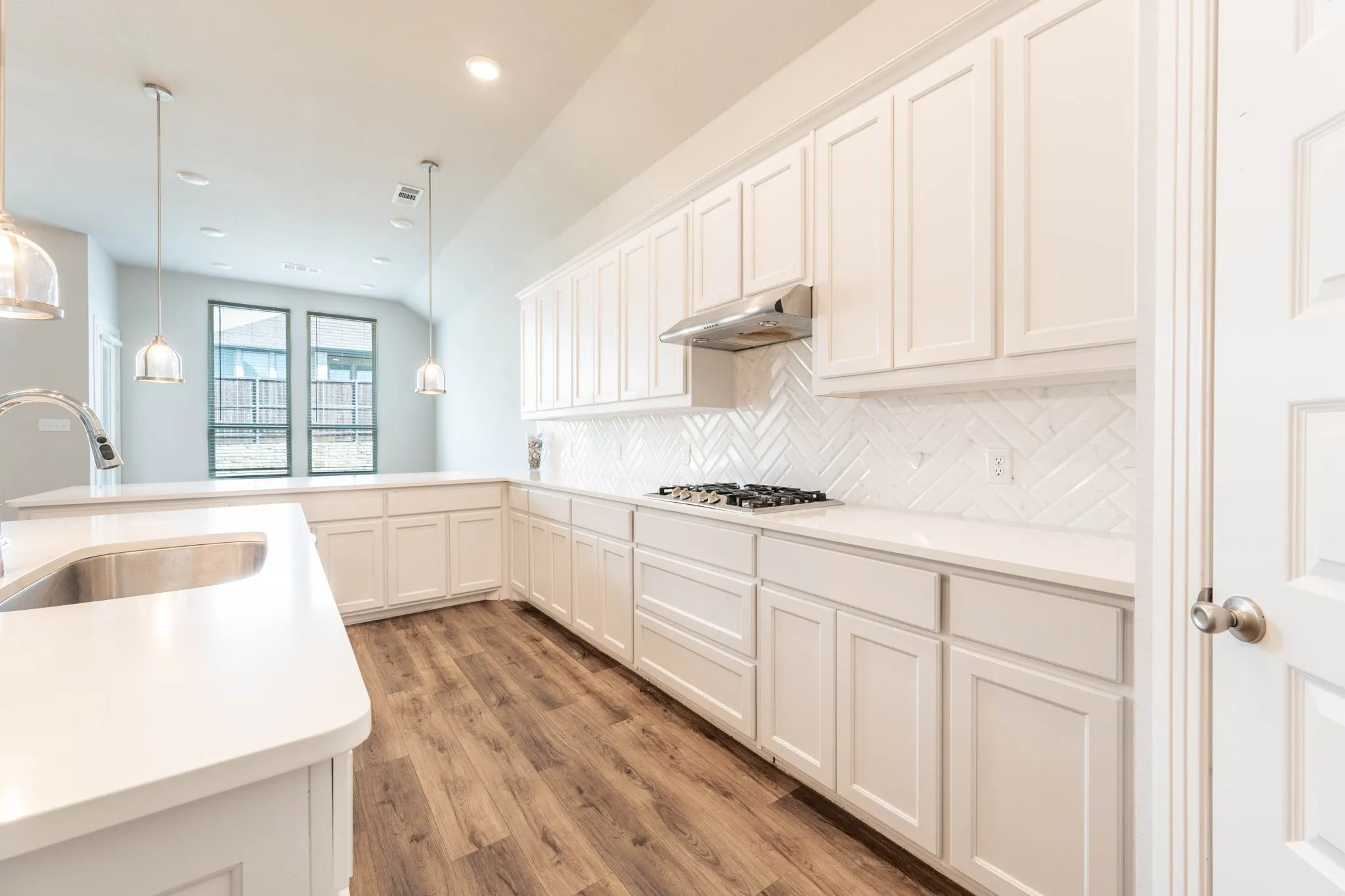 White cabinetry, stainless steel sink, wood-finish flooring, white countertops, and white herringbone tile backsplash