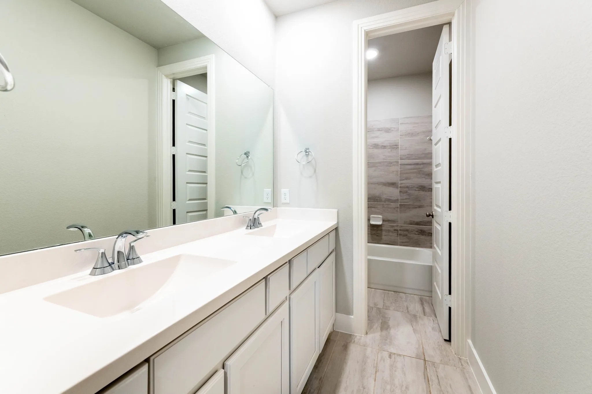 Dual vanity with integrated sinks, chrome fixtures, white cabinetry, and a large wall mirror