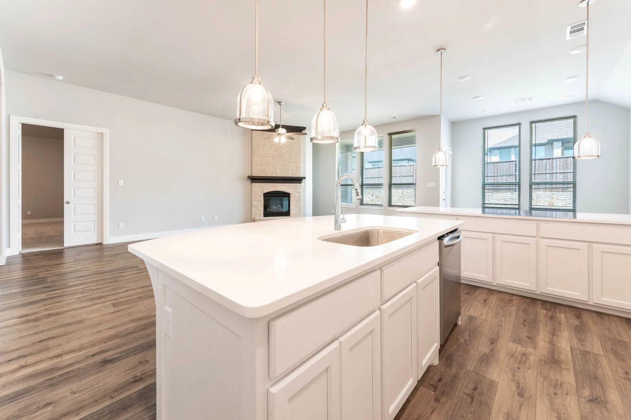 Kitchen island with a built-in sink, stainless steel dishwasher, and pendant lighting, wood-finish flooring, white cabinetry, and a stone fireplace
