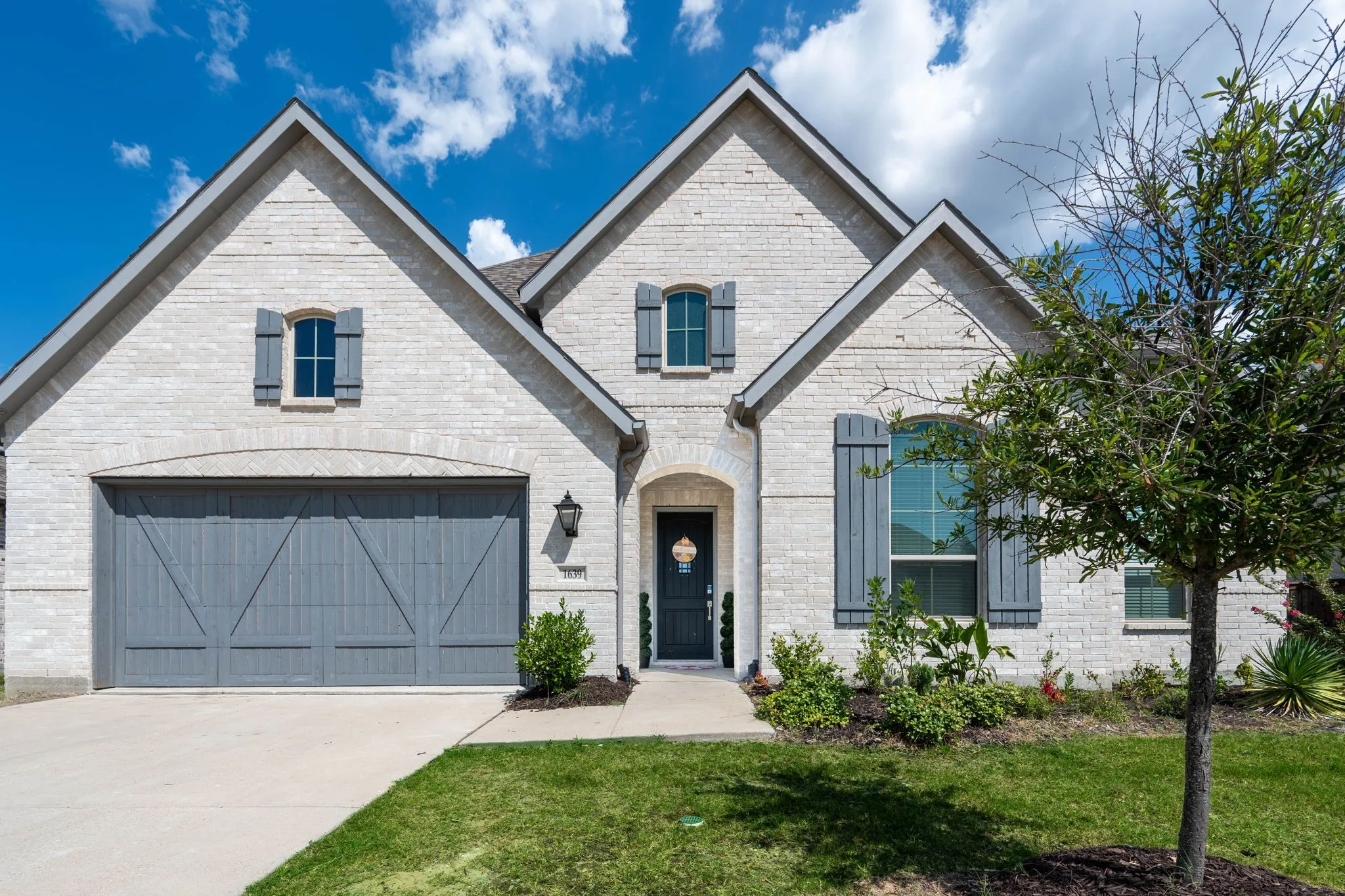 White brick exterior with gray gabled accents, featuring a two-car garage with a panel door