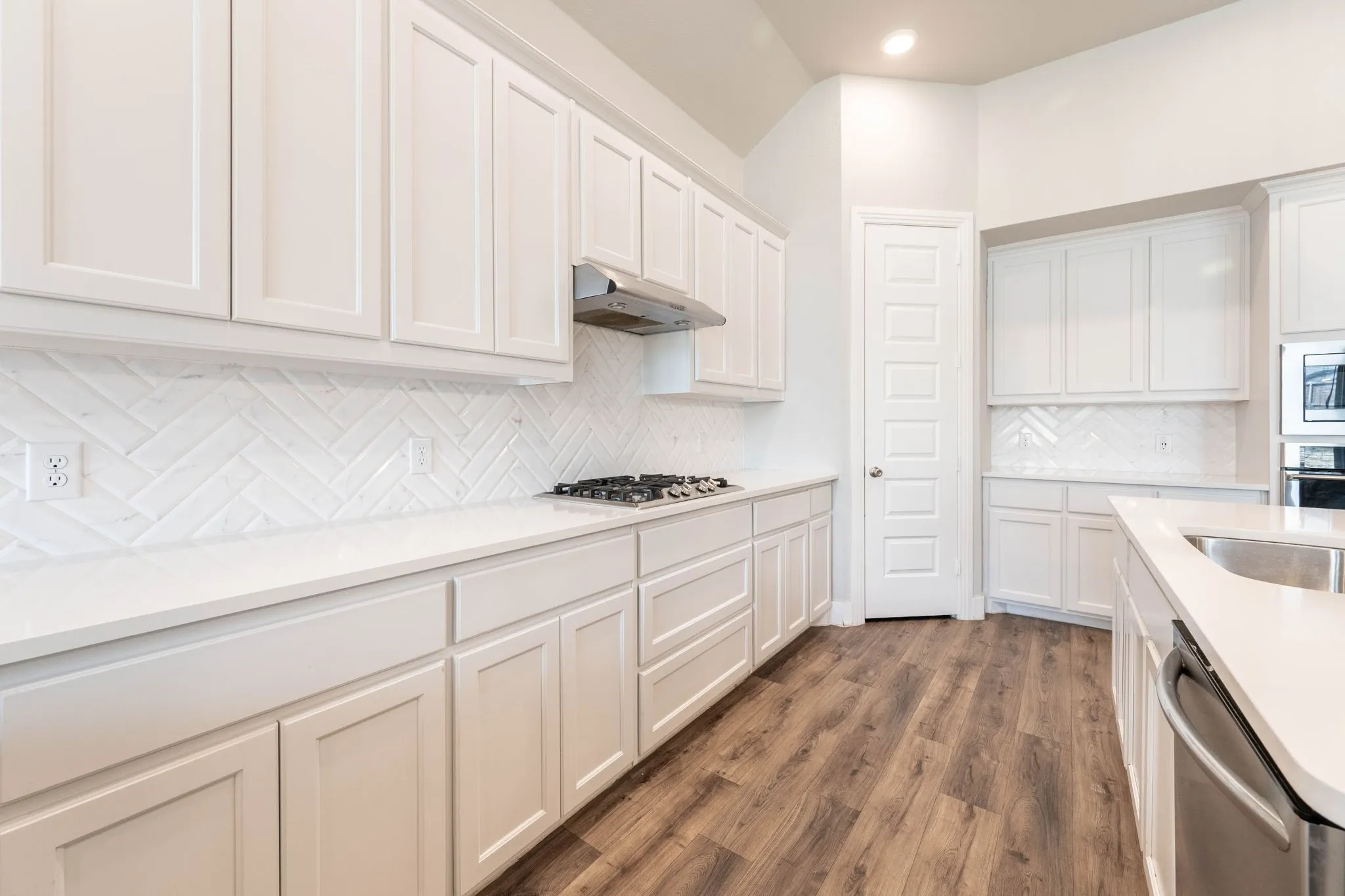 White shaker cabinetry, herringbone tile backsplash, white countertops, wood-finish flooring, and a stainless steel gas range