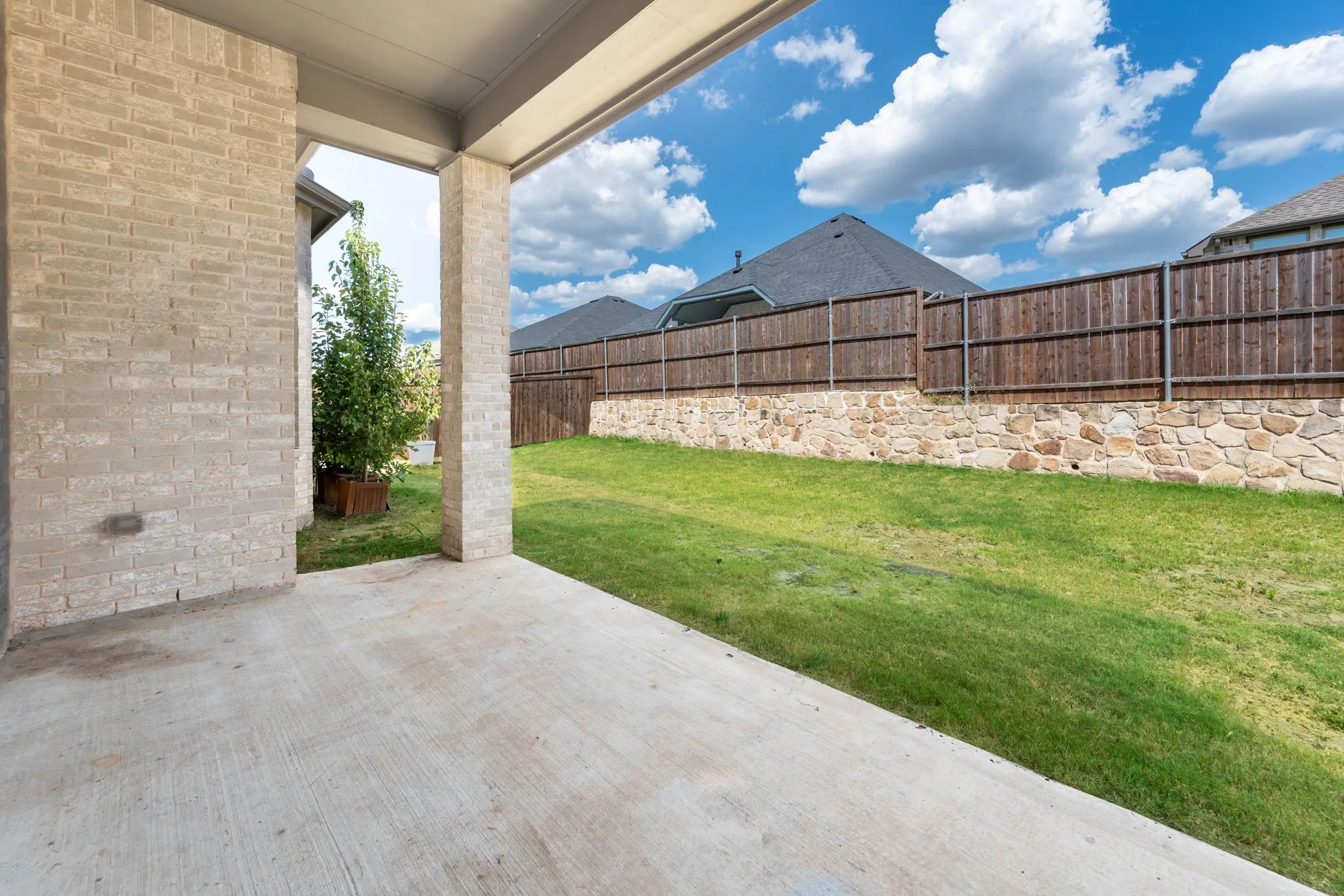 Covered patio with a concrete surface, a manicured lawn, a stone retaining wall, and a wood privacy fence