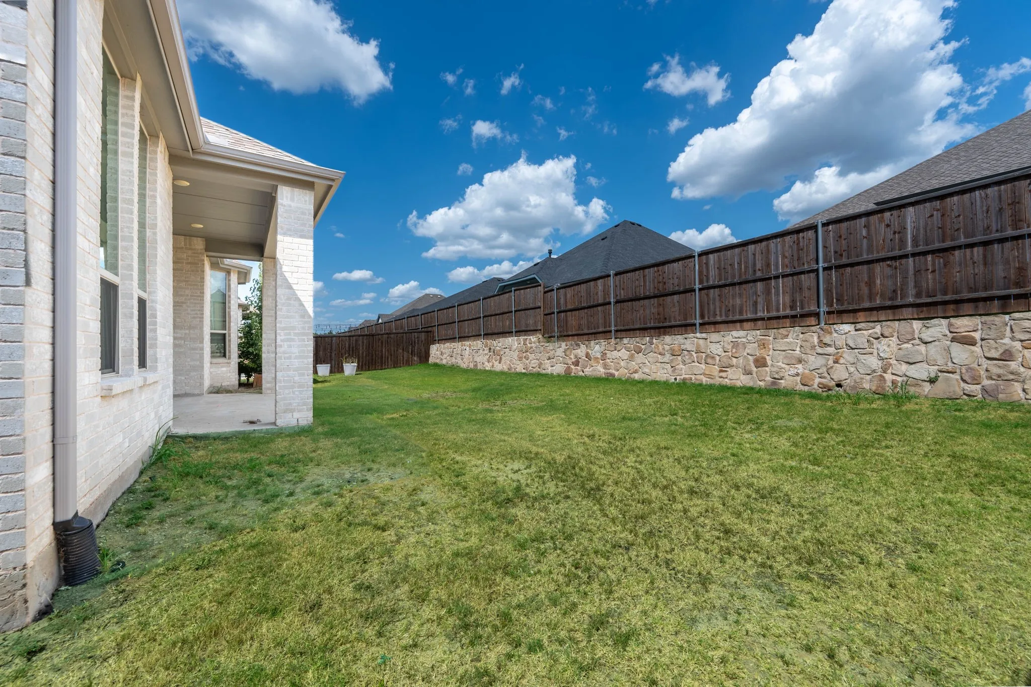 Expansive backyard featuring a manicured lawn, stone retaining wall, and wood privacy fence