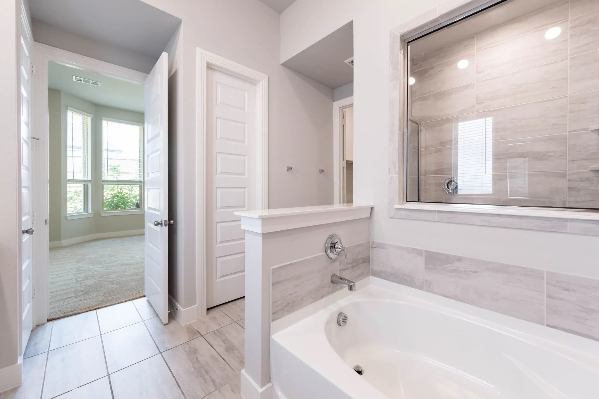 Soaking tub with chrome fixtures, tiled surround, and glass-enclosed shower