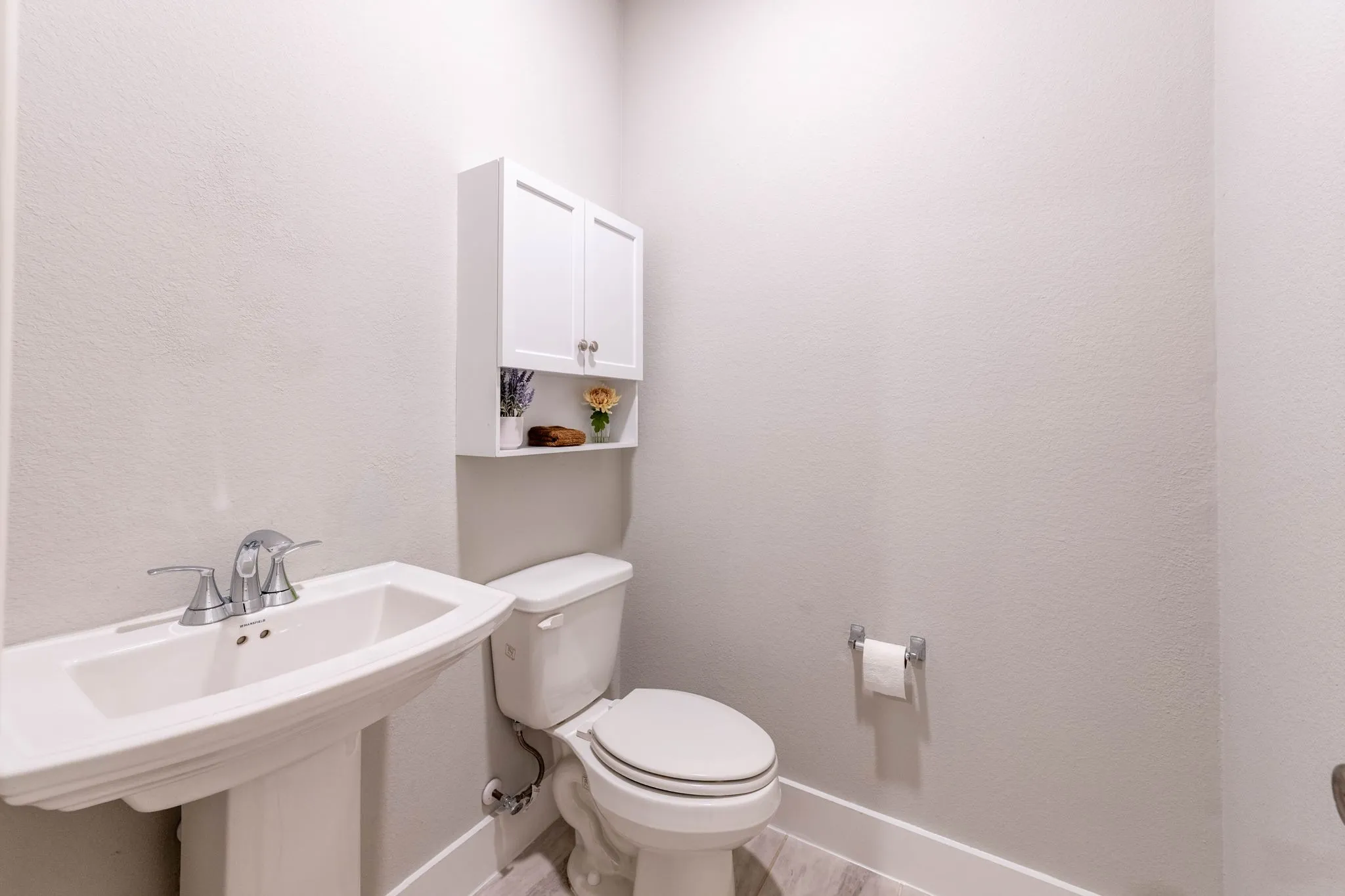 Pedestal sink with chrome faucet, wall-mounted storage cabinet, and wood-finish flooring