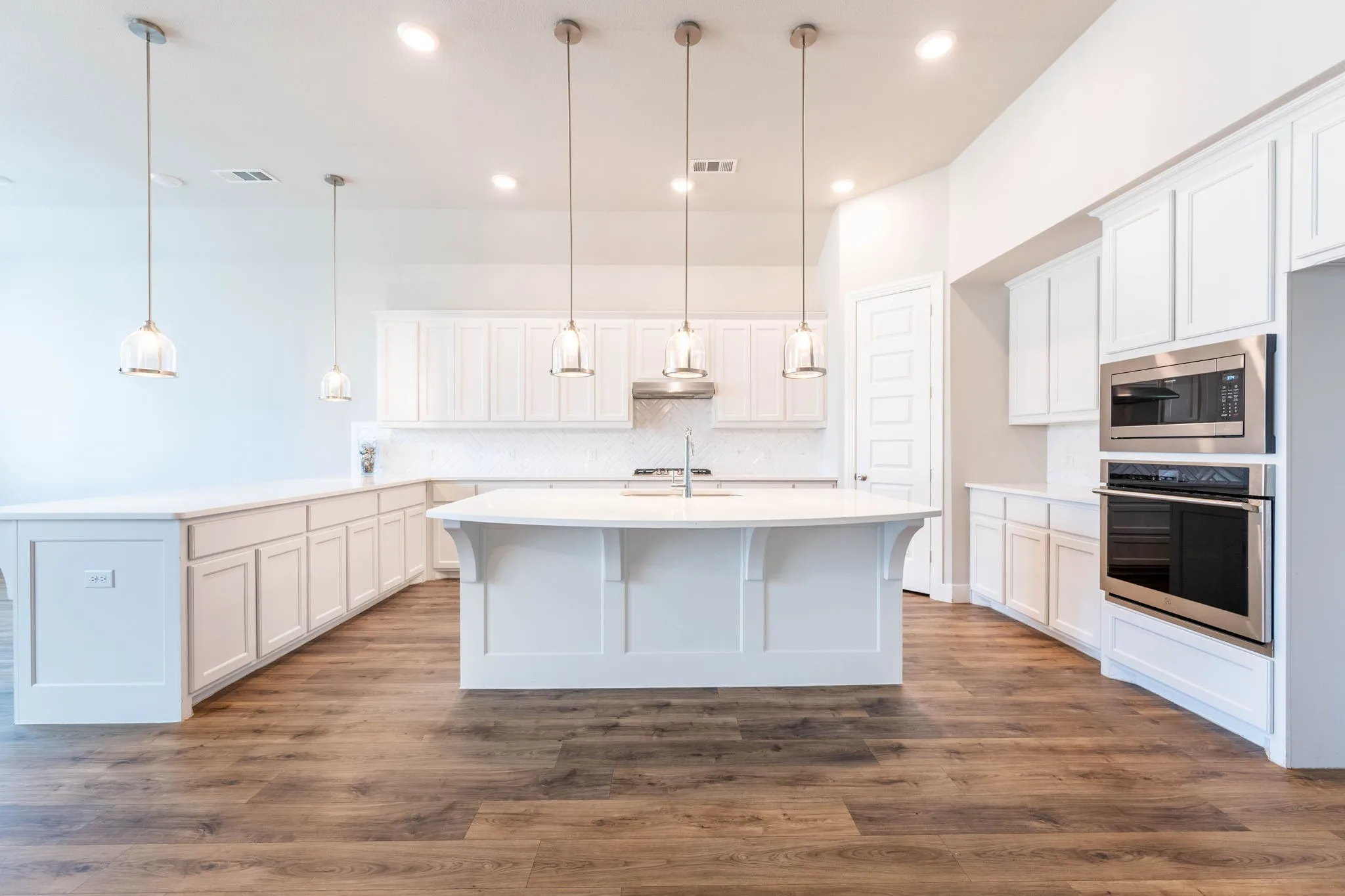 White cabinetry, wood-finish flooring, recessed lighting, central island, and stainless steel appliances
