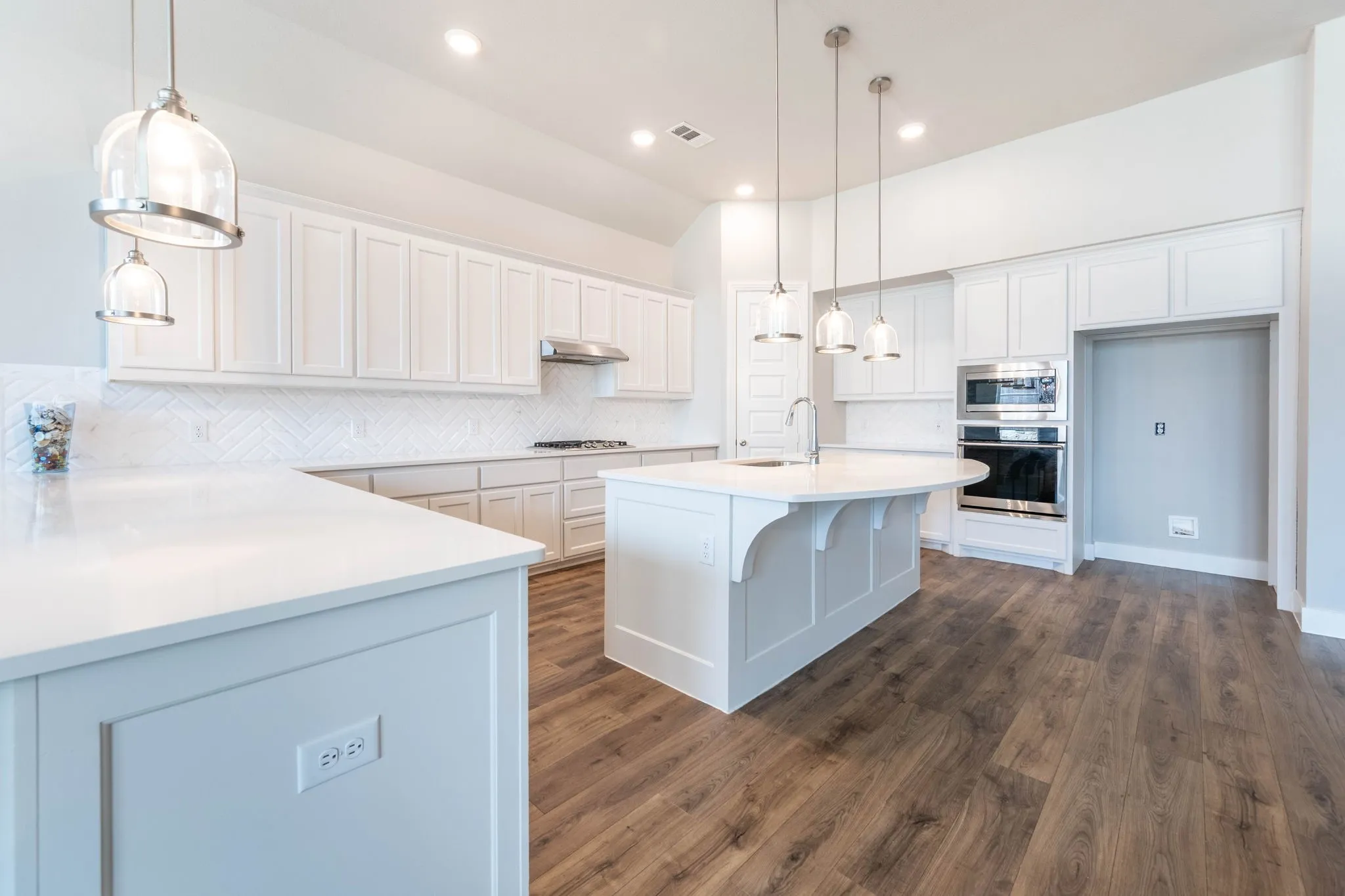 Spacious kitchen featuring an expansive island, light-toned cabinetry, stainless steel appliances, wood-finish flooring, and pendant lighting