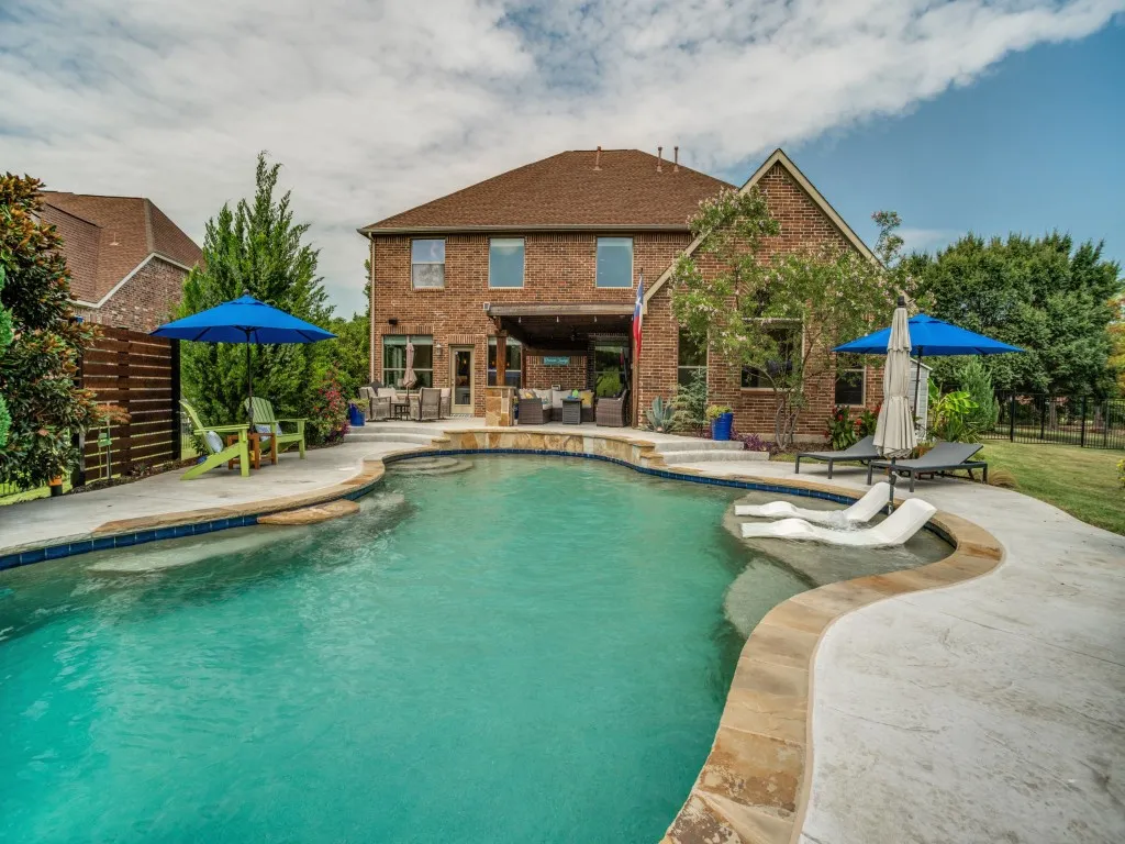 Resort-style backyard featuring a private saltwater pool with tanning ledge and margarita table, multiple seating areas and covered outdoor living at this Flower Mound home.