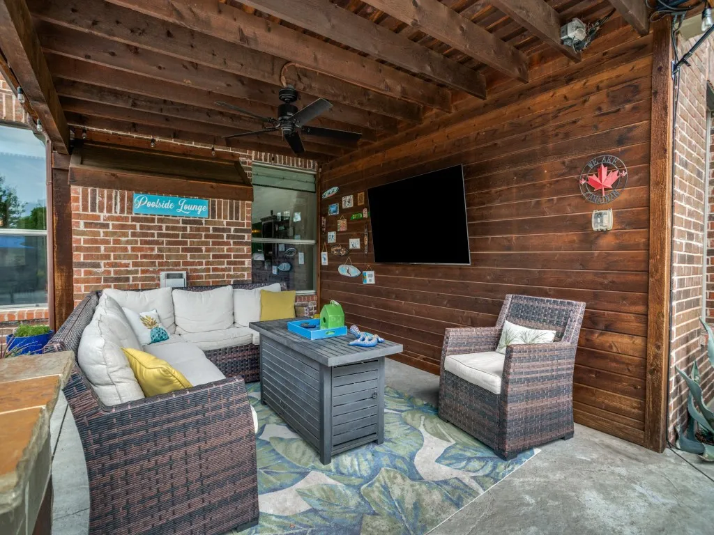Covered outdoor living area with TV, ceiling fan and comfortable lounge space overlooking the private backyard and pool—perfect for year-round entertaining.