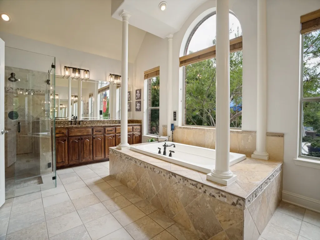 Spa-like primary bathroom featuring a jetted tub, separate shower, dual vanities and abundant natural light.