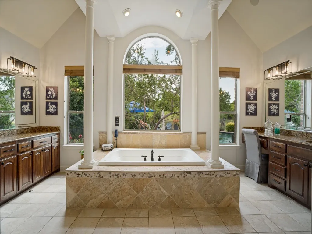Generous primary bath with jetted soaking tub, separate vanities, abundant cabinetry and a dramatic arched window overlooking the private backyard.