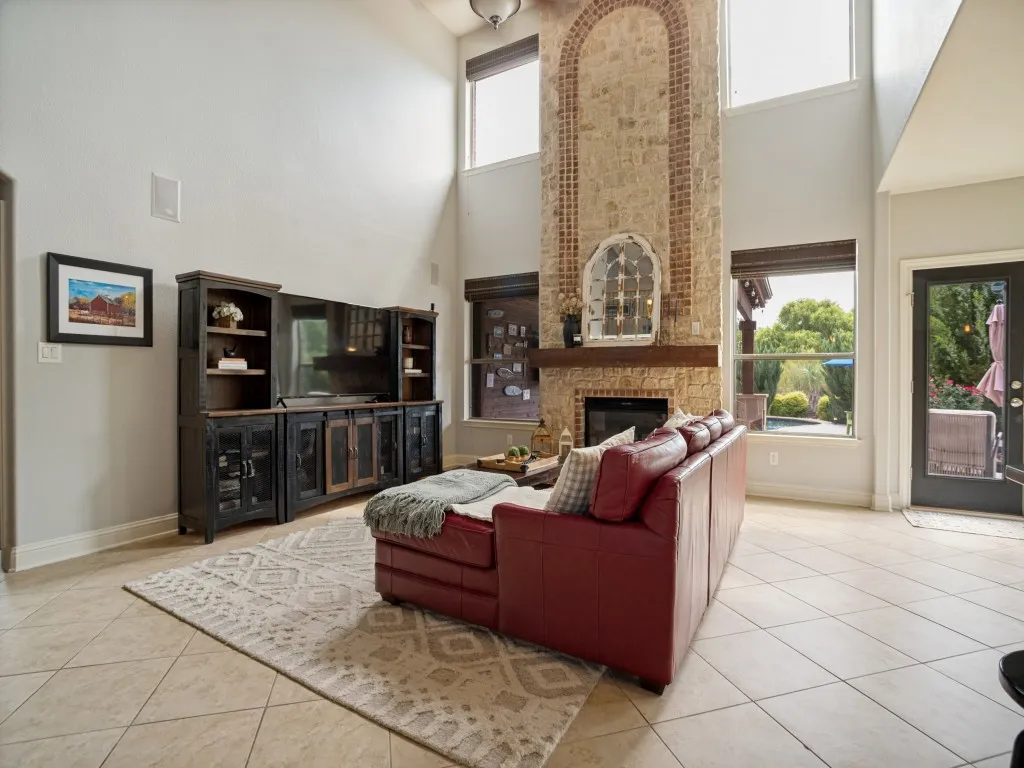 Dramatic two-story family room featuring a floor-to-ceiling stone fireplace, soaring ceilings and views of the private pool and landscaped backyard.