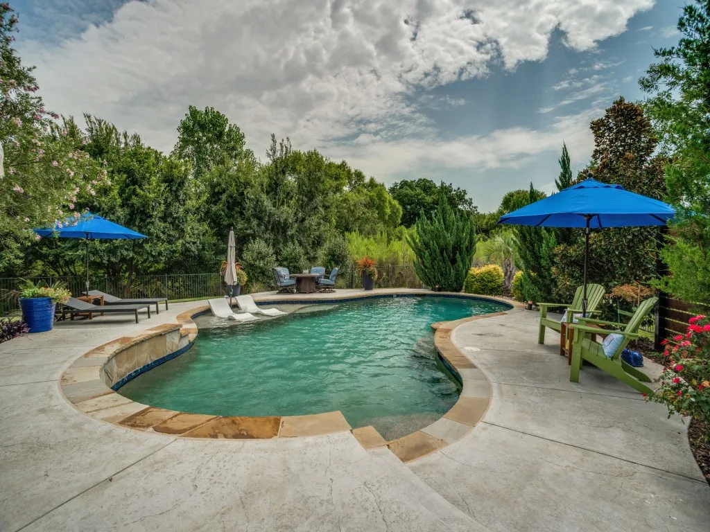 Resort-style saltwater pool with tanning ledge and margarita table surrounded by lush landscaping in this private Flower Mound backyard retreat.
