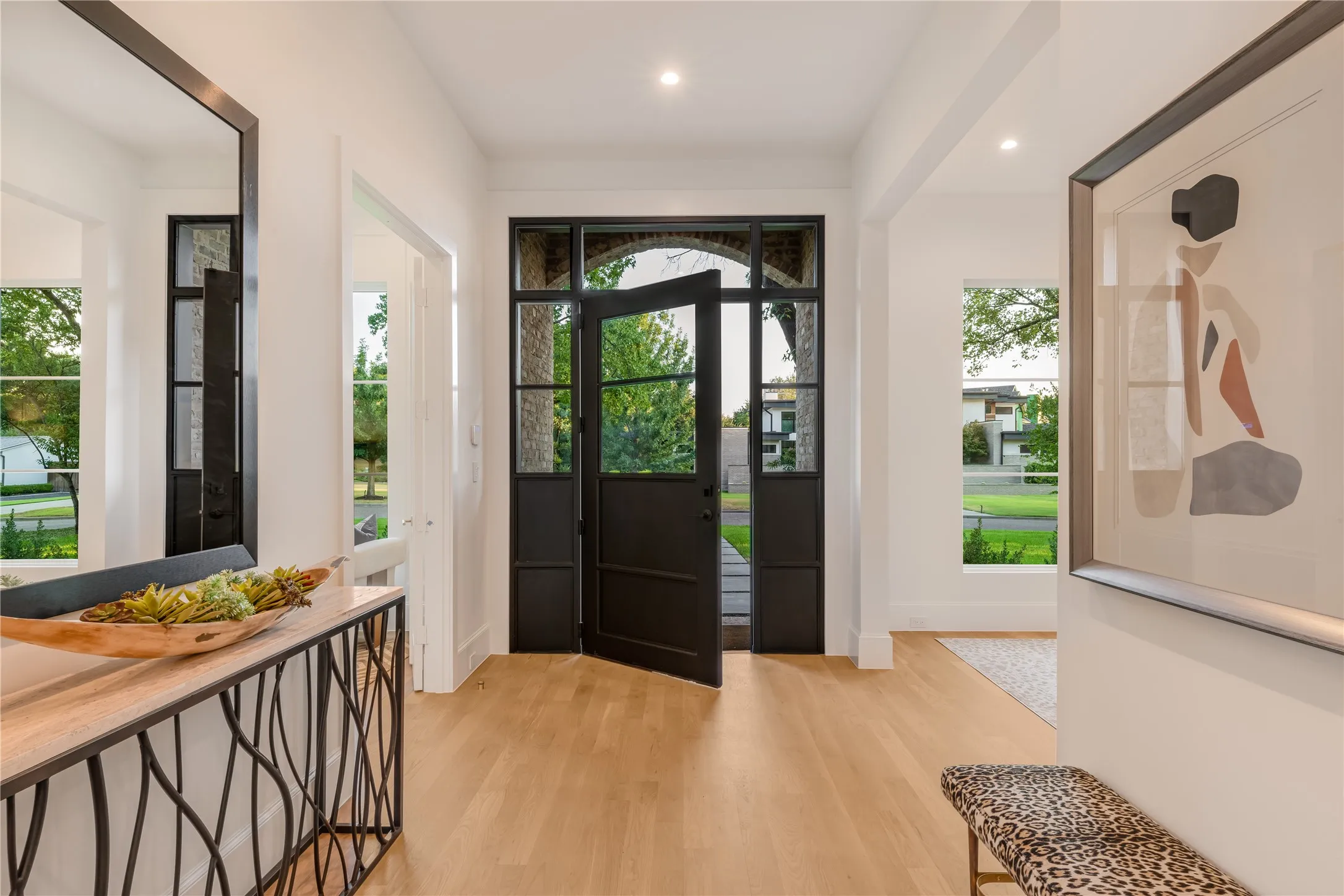 Arched iron-frame entry doors, light wood-finish flooring, recessed lighting, and a console table with an organic iron base