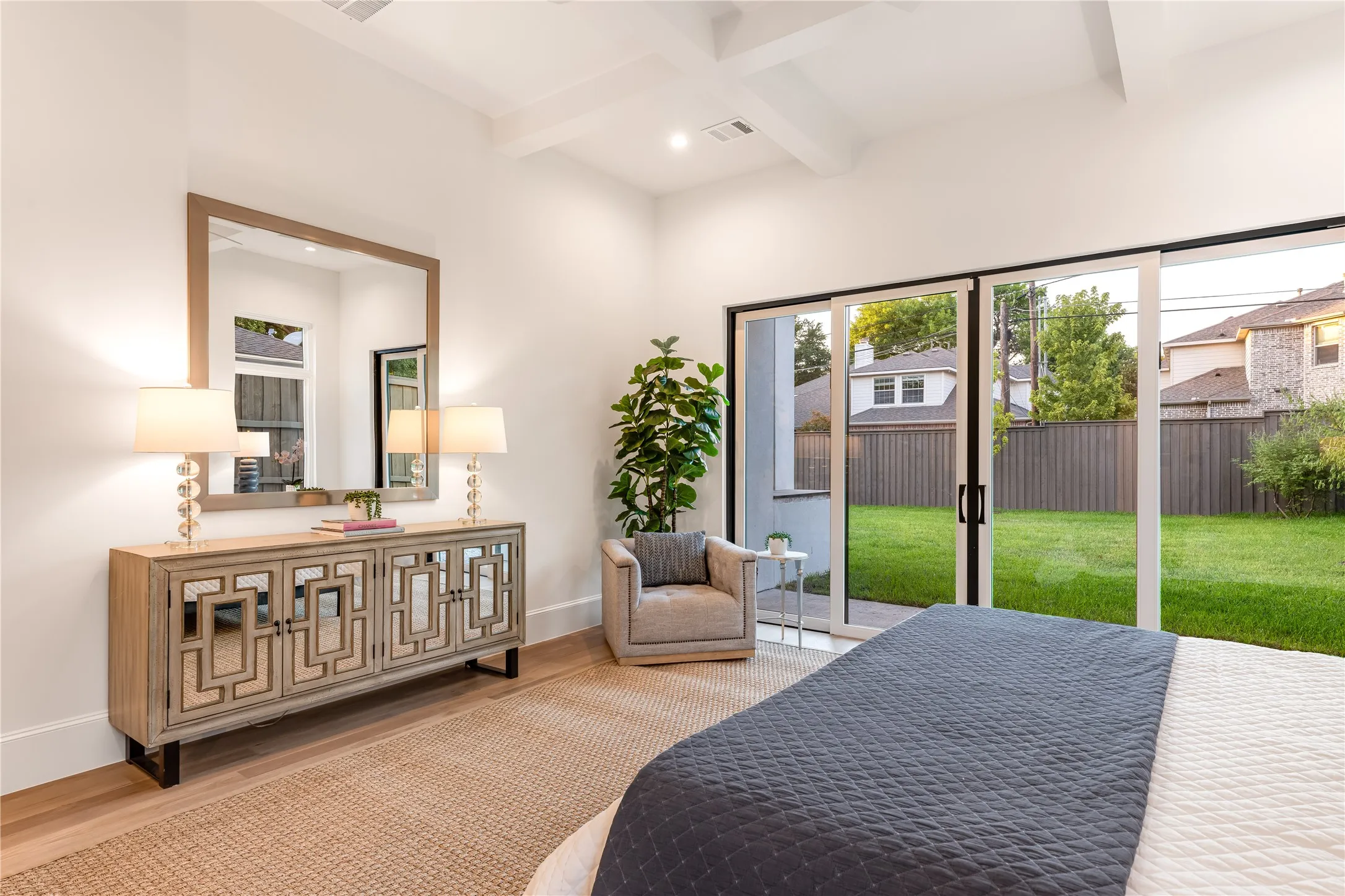 Vaulted ceiling with exposed beams, wood-finish flooring, sliding glass patio doors, and a spacious green yard