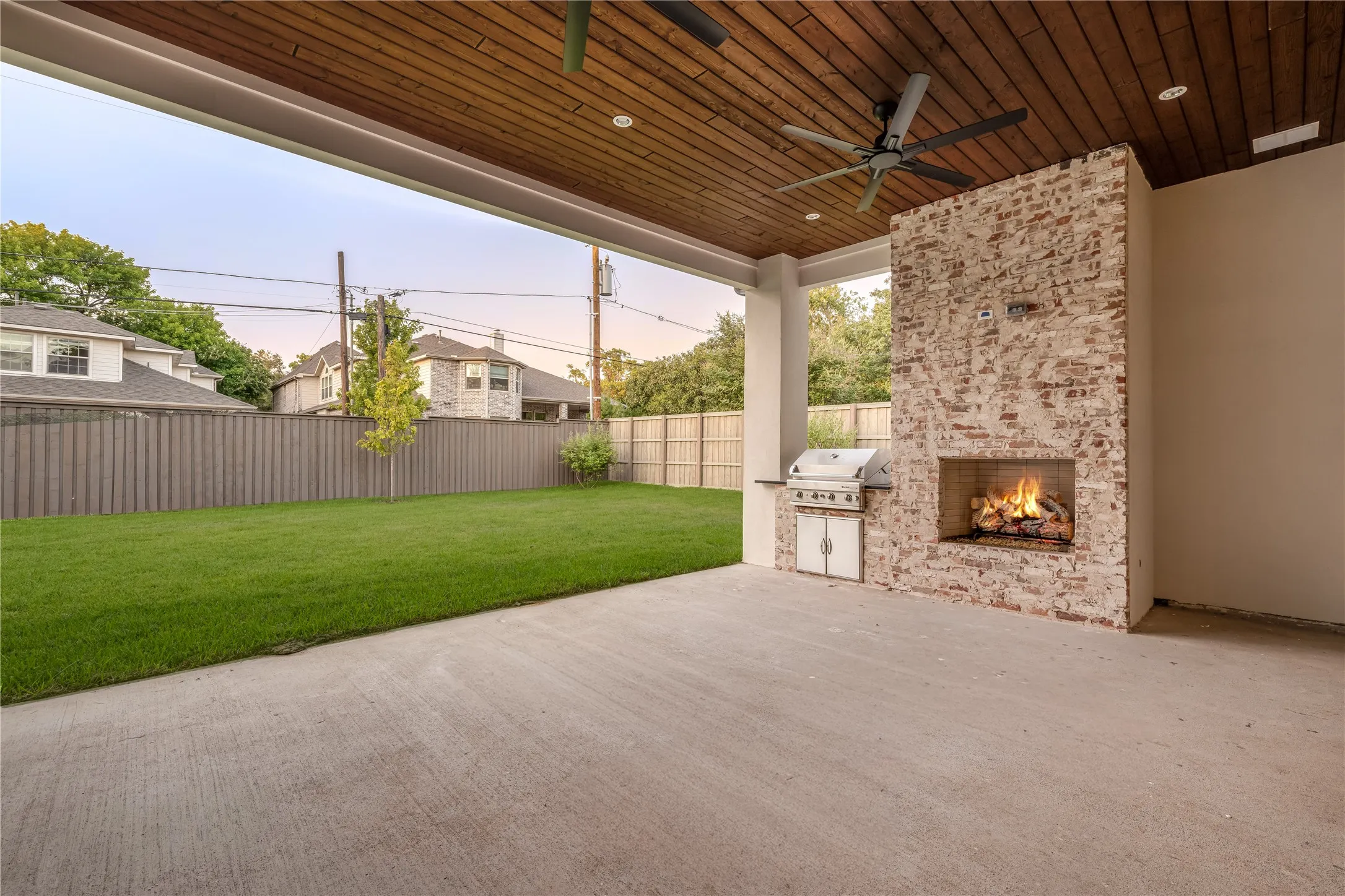 Expansive covered patio with a wood-finish plank ceiling, two ceiling fans, and a brick fireplace