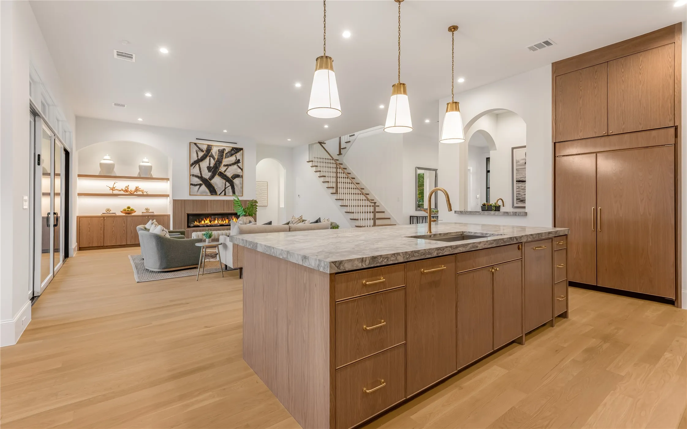 Open-concept living area with wood-finish flooring, a kitchen island featuring a sink, and integrated wood-finish cabinetry