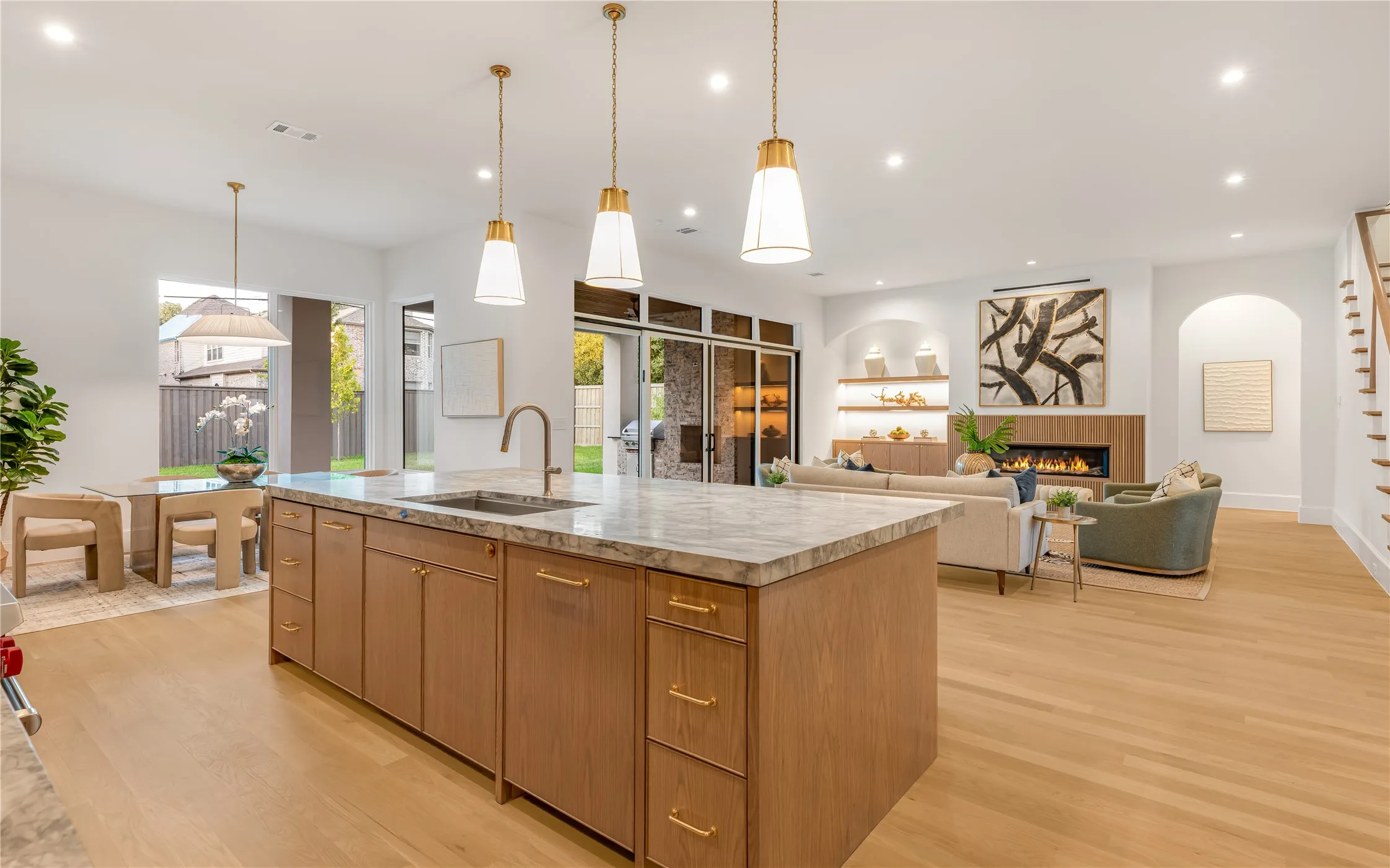Spacious open-concept living area featuring a large kitchen island with a stone countertop, light wood-finish flooring, and recessed lighting