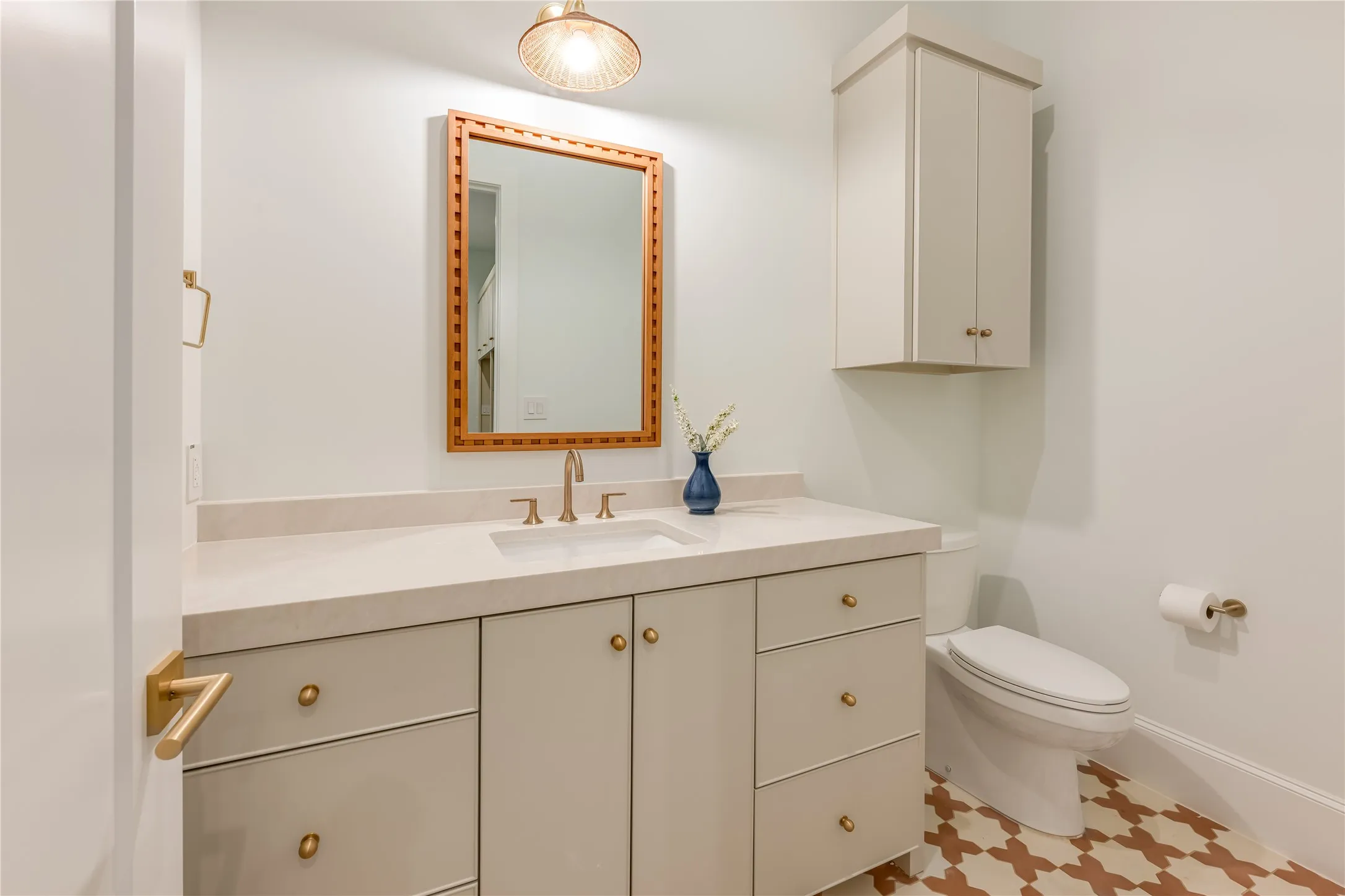 Vanity with integrated sink, rectangular mirror with a decorative frame, wall-mounted upper cabinetry, and patterned floor tiling