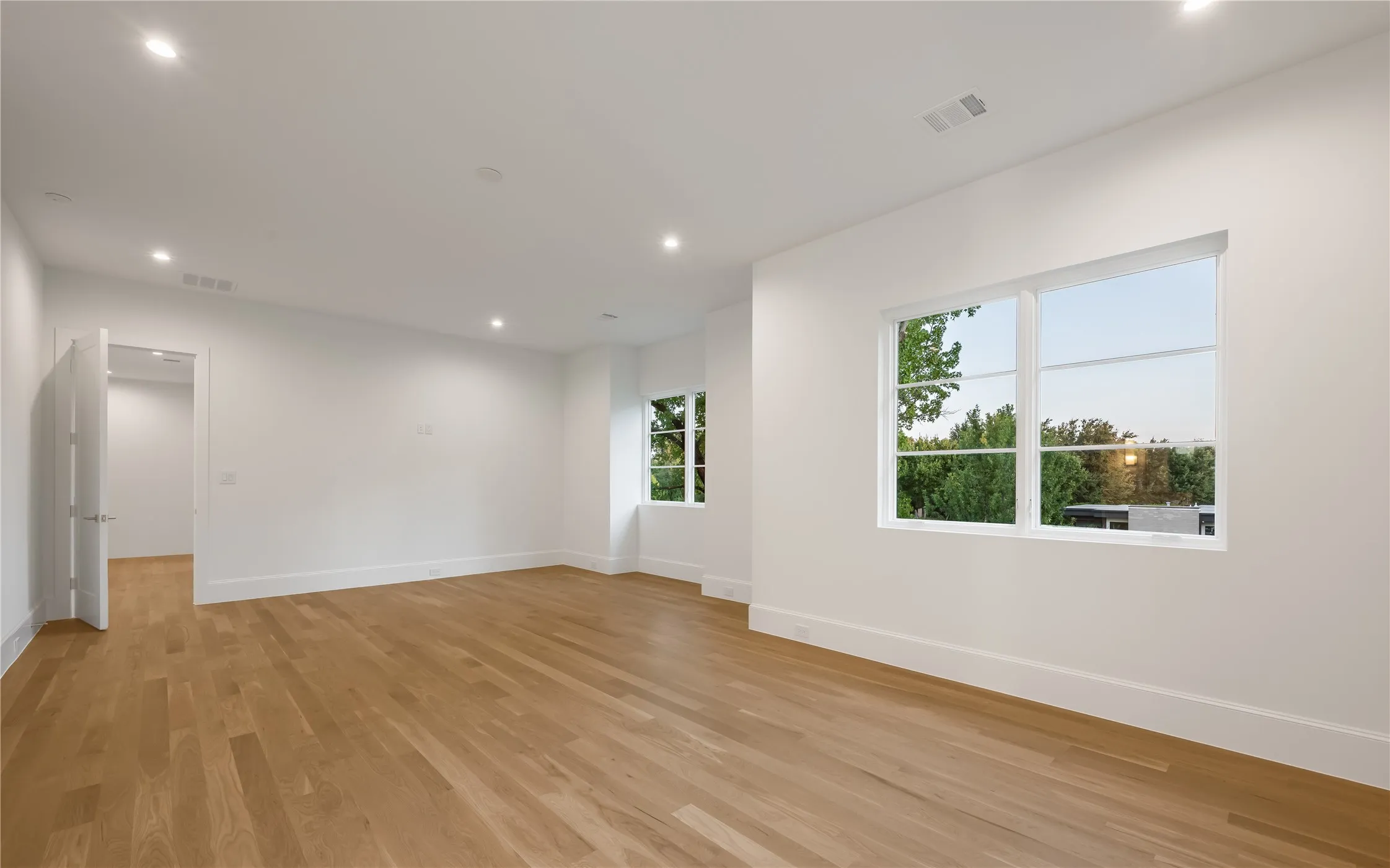 Spacious room with wood-finish flooring, recessed lighting, white walls, and multiple windows
