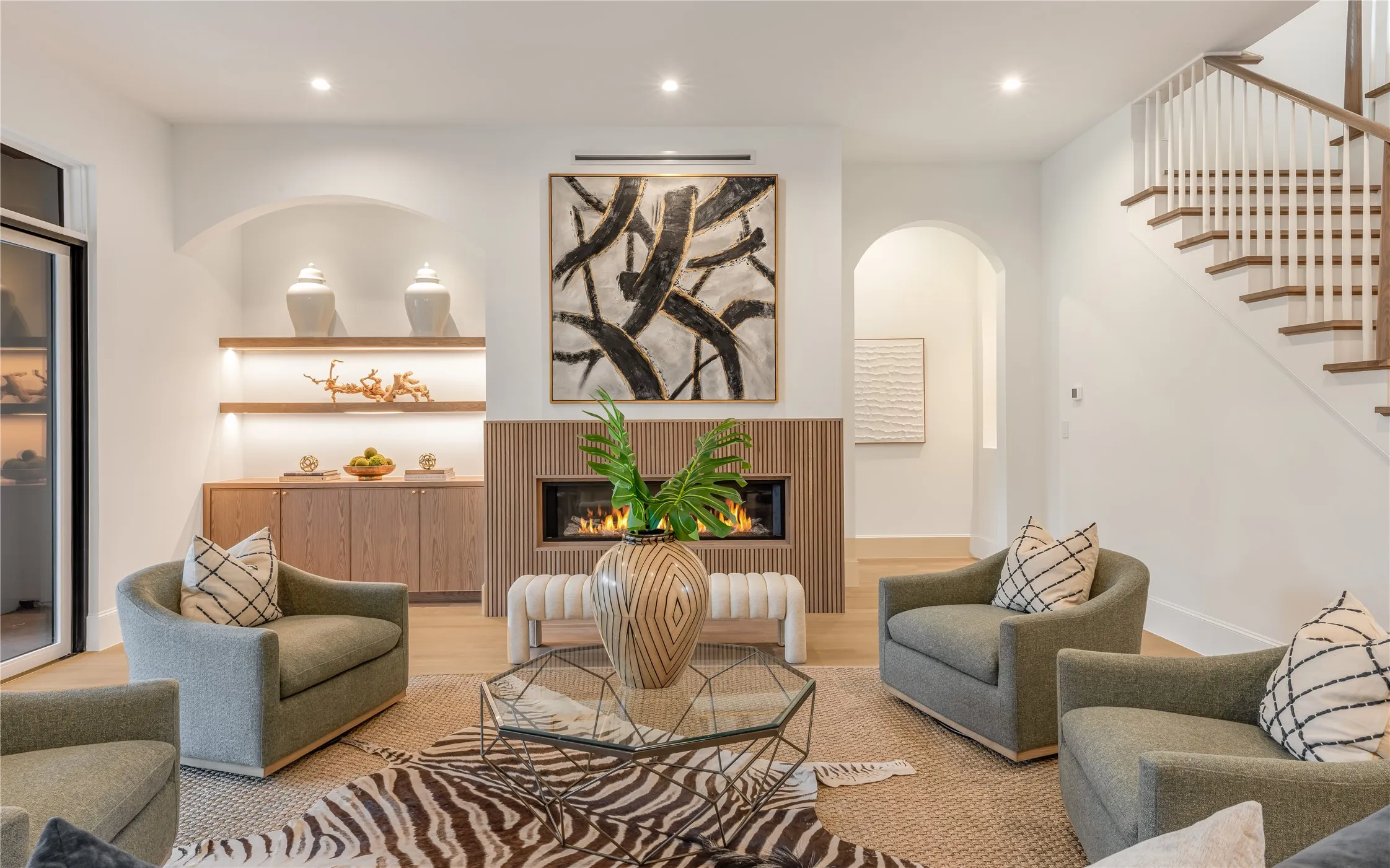 Built-in cabinetry with illuminated shelving, a linear fireplace with wood-finish surround, hardwood flooring, and a hardwood staircase with white risers