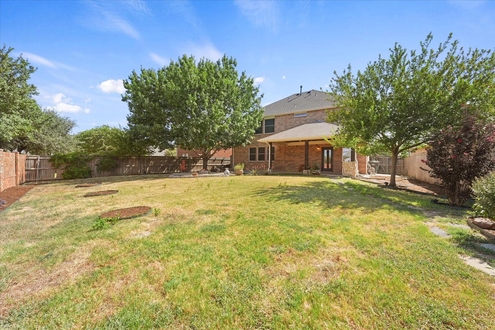 Expansive backyard featuring mature trees, a covered patio, brick exterior, and a privacy fence