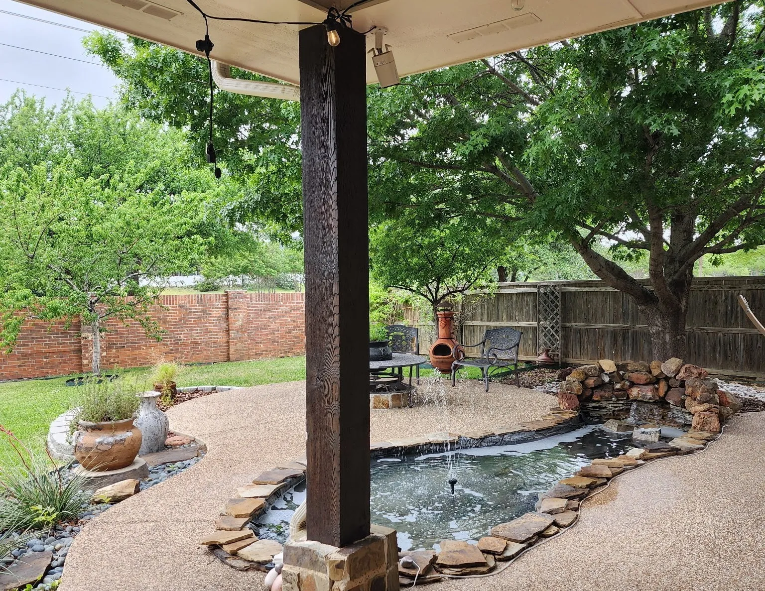 Expansive backyard featuring a brick privacy fence, stone-edged planting beds, a natural stone pathway, and mature trees, creating a private and inviting outdoor retreat.