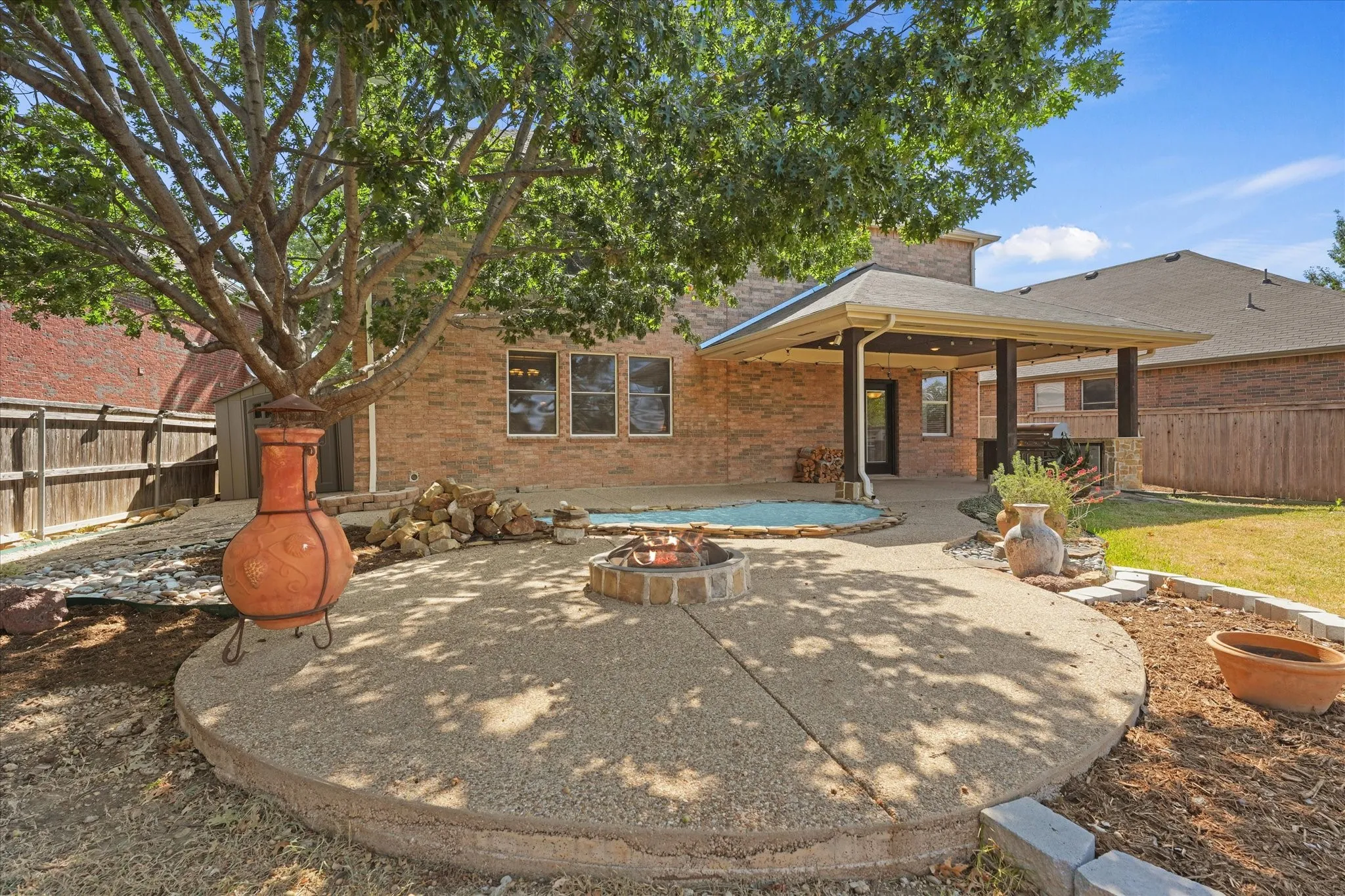 Covered patio with exposed aggregate,  integrated outdoor kitchen, recessed lighting, and brick exterior, creating an inviting outdoor retreat ideal for entertaining. Enjoy the tranquil water feature, expansive sidewalks, and fireplace, perfect for relaxing or gathering with family and​​‌​​​​‌​​‌‌​‌‌​​​‌‌​‌​‌​‌​​​‌​​ friends.