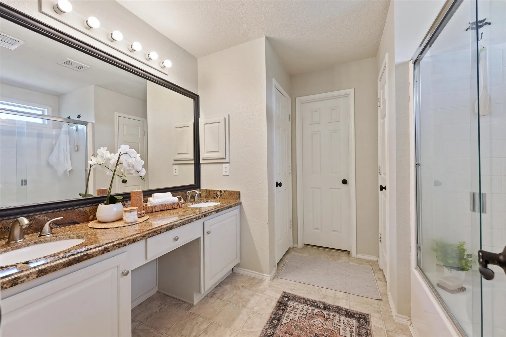 Double vanity with integrated sinks, granite countertop, large framed mirror, and glass-enclosed shower