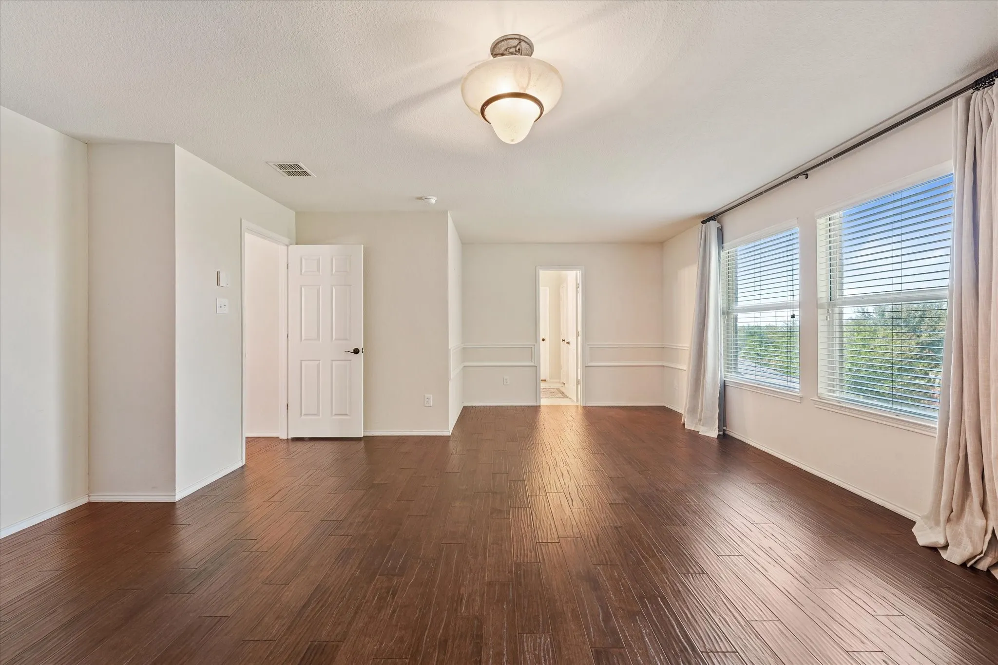 Spacious primary bedroom with room for a sitting area, featuring neutral carpeting, white walls, a vaulted ceiling with decorative chandelier, crown molding, and a partial textured accent wall. The ensuite bath and gigantic walk-in closet add comfort and convenience.