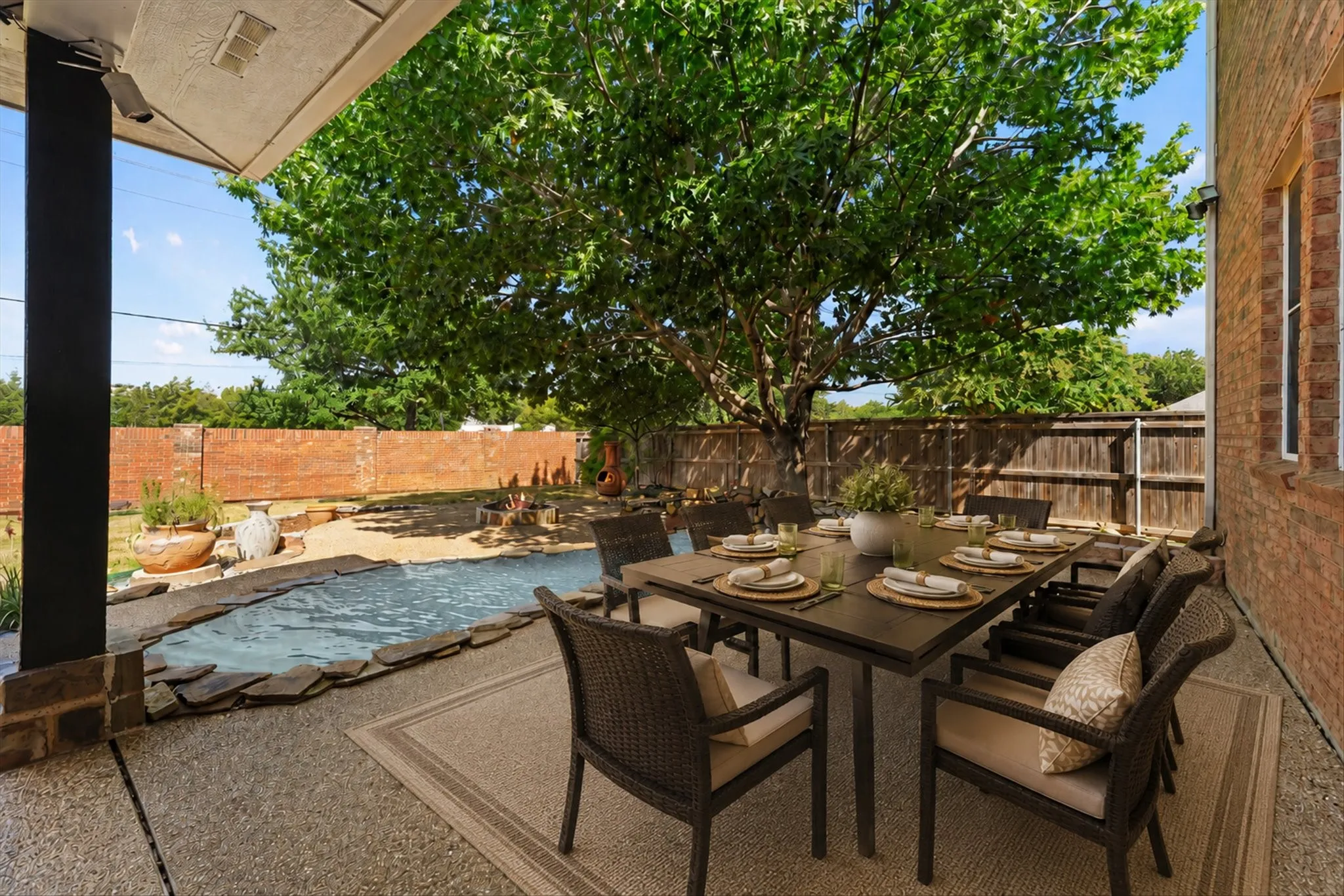 Covered patio with integrated outdoor kitchen, recessed lighting, and brick exterior, creating an inviting outdoor retreat ideal for entertaining. Enjoy the tranquil water feature, expansive sidewalks, and fireplace, perfect for relaxing or gathering with family and friends.