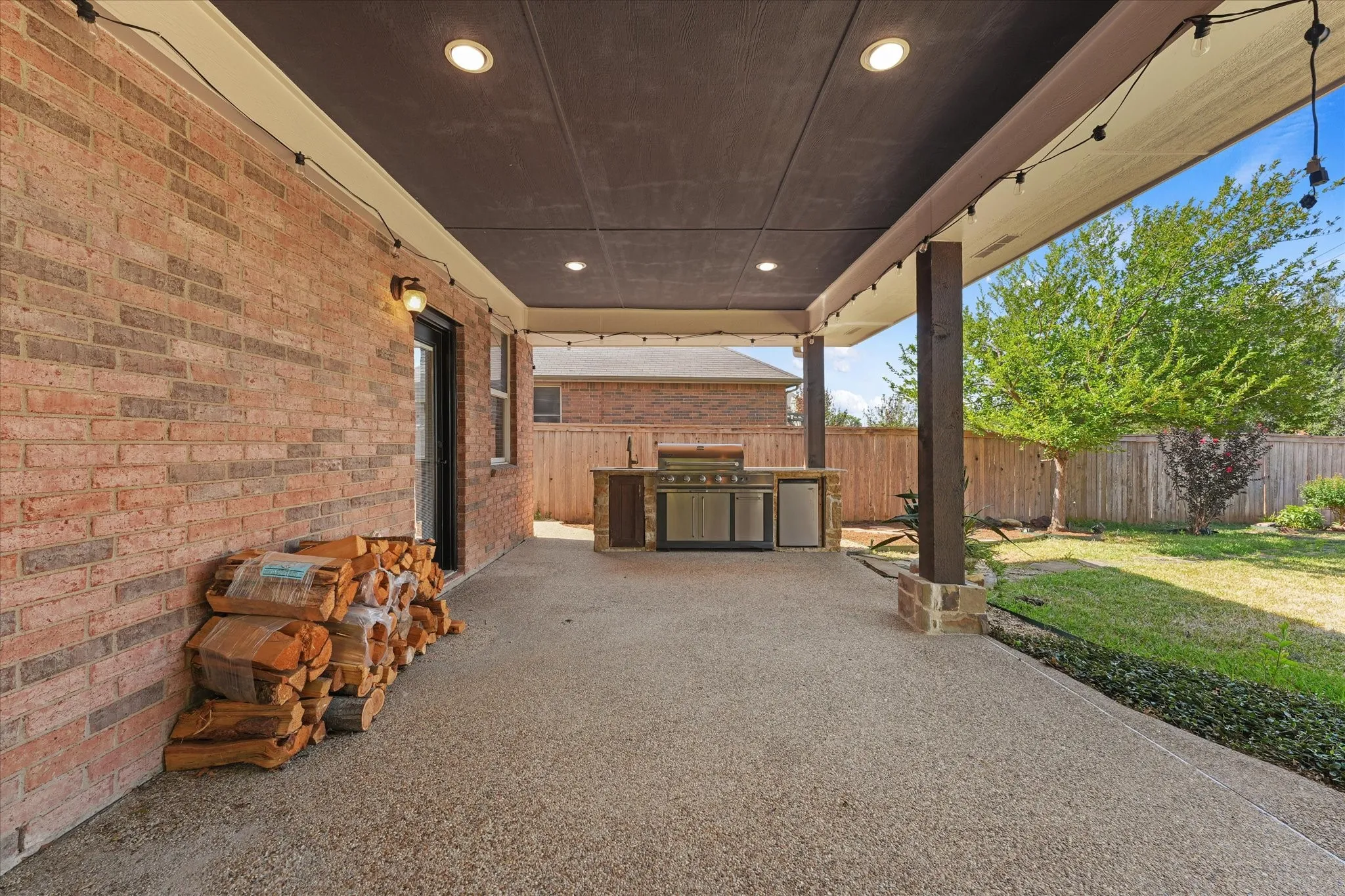 Covered patio with integrated outdoor kitchen, recessed lighting, and brick exterior, creating an inviting outdoor retreat ideal for entertaining. Enjoy the tranquil water feature, expansive sidewalks, and fireplace, perfect for relaxing or gathering with family and friends.