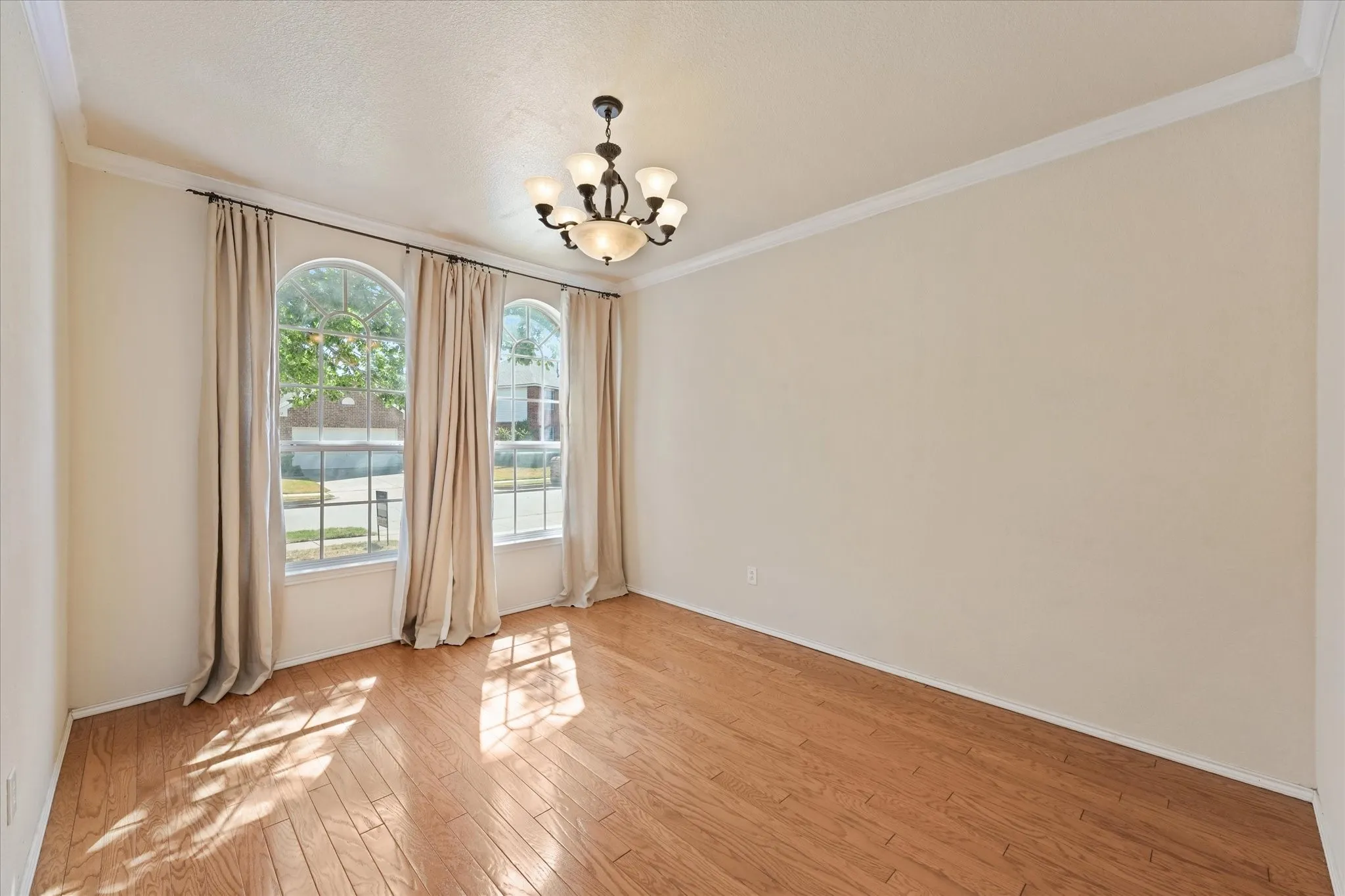 Arch-top windows with drapes, wood-finish flooring, crown molding, and a chandelier lighting fixture create an inviting flex space off of the entry to use as an office, play room or multiple other uses.