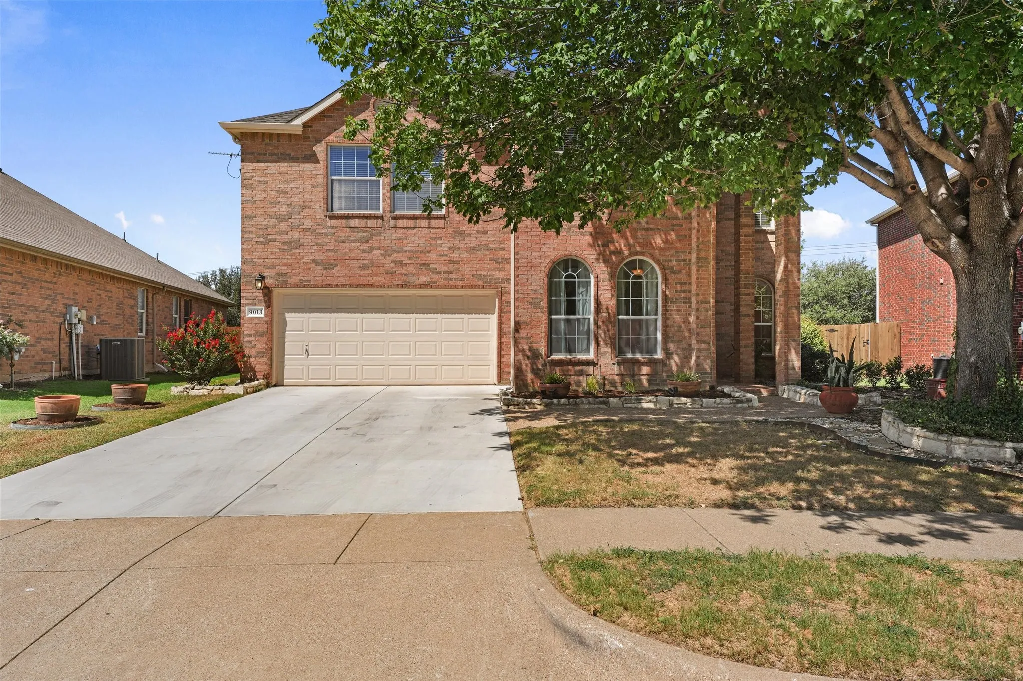 Brick exterior with arched windows, an attached two-car garage, concrete driveway, and mature landscaping