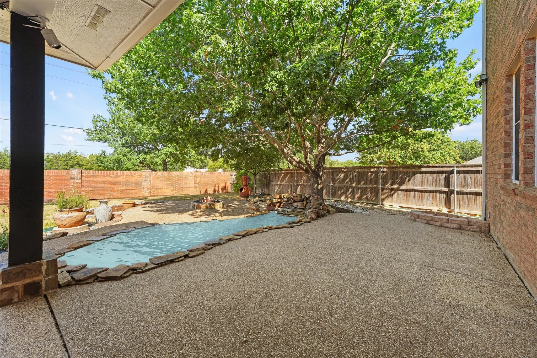 Expansive backyard featuring a brick privacy fence, stone-edged planting beds, a natural stone pathway, and mature trees, creating a private and inviting outdoor retreat.