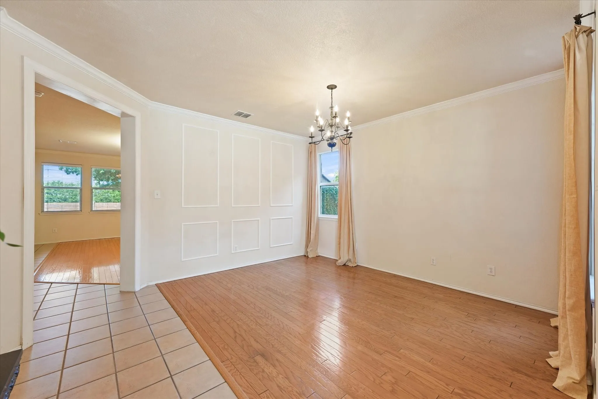 Arch-top windows with drapes, wood-finish flooring, picture frame and crown molding, and a chandelier lighting fixture create an inviting dining area to host large gatherings. Seamless flow into family room, kitchen and front flex room give ample space for entertaining.