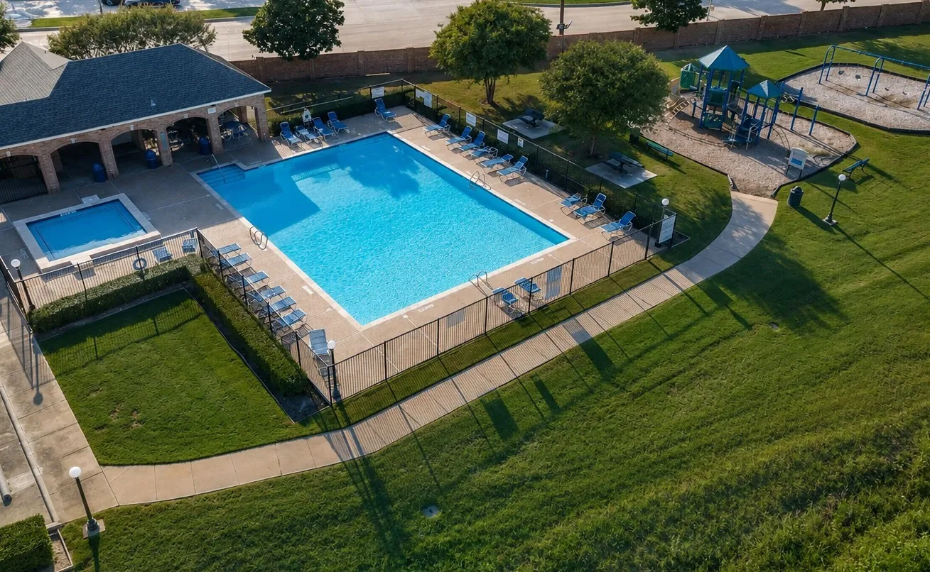 Community swimming pool, separate wading pool, adjacent clubhouse structure, paved pathways, and playground area