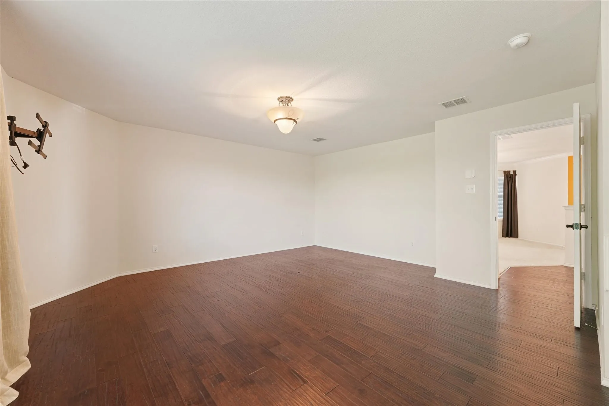 Spacious primary bedroom with room for a sitting area, featuring neutral carpeting, white walls, a vaulted ceiling with decorative chandelier, crown molding, and a partial textured accent wall. The ensuite bath and gigantic walk-in closet add comfort and convenience.