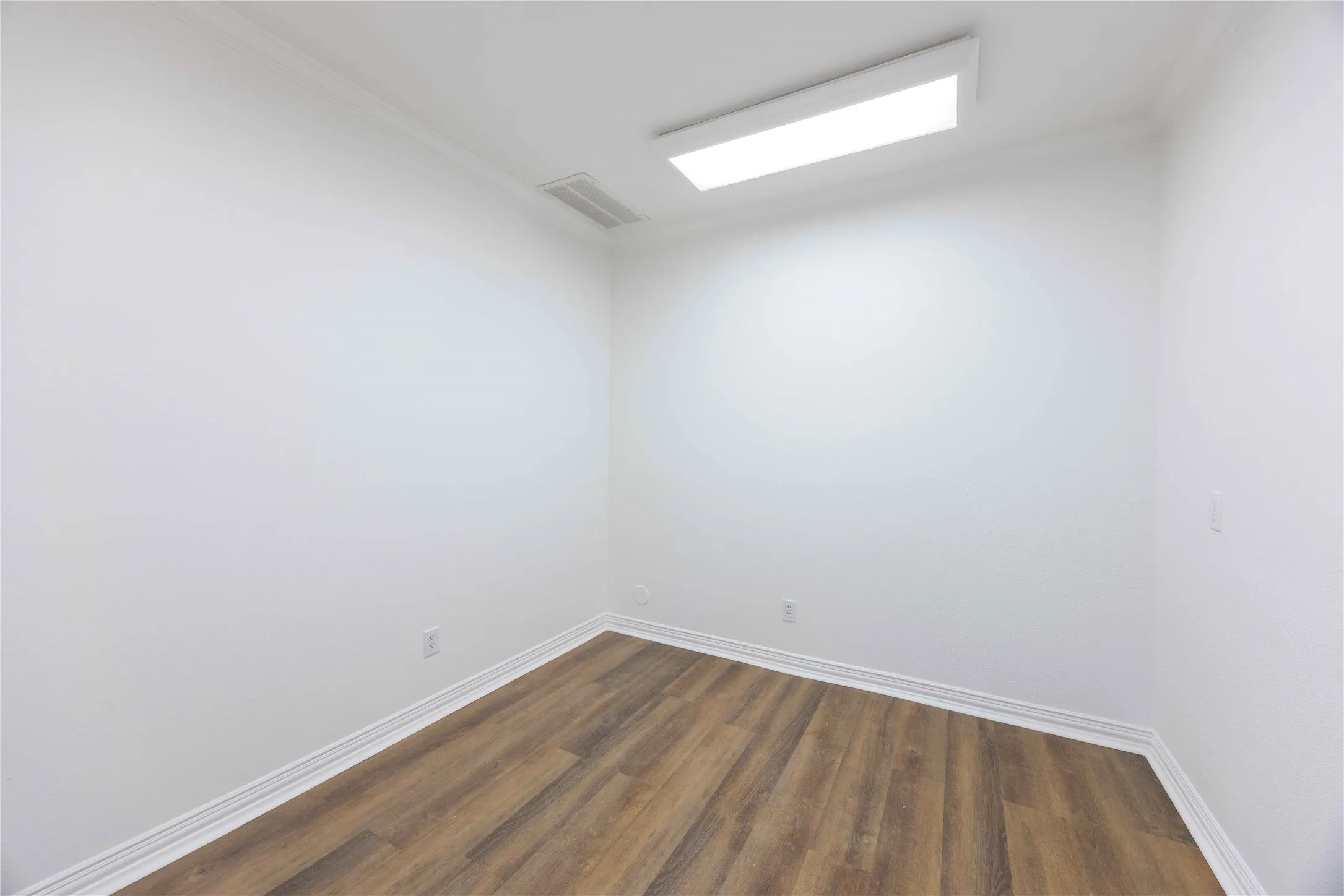 Recessed rectangular ceiling light, wood-finish flooring, white walls, white trim, and crown molding