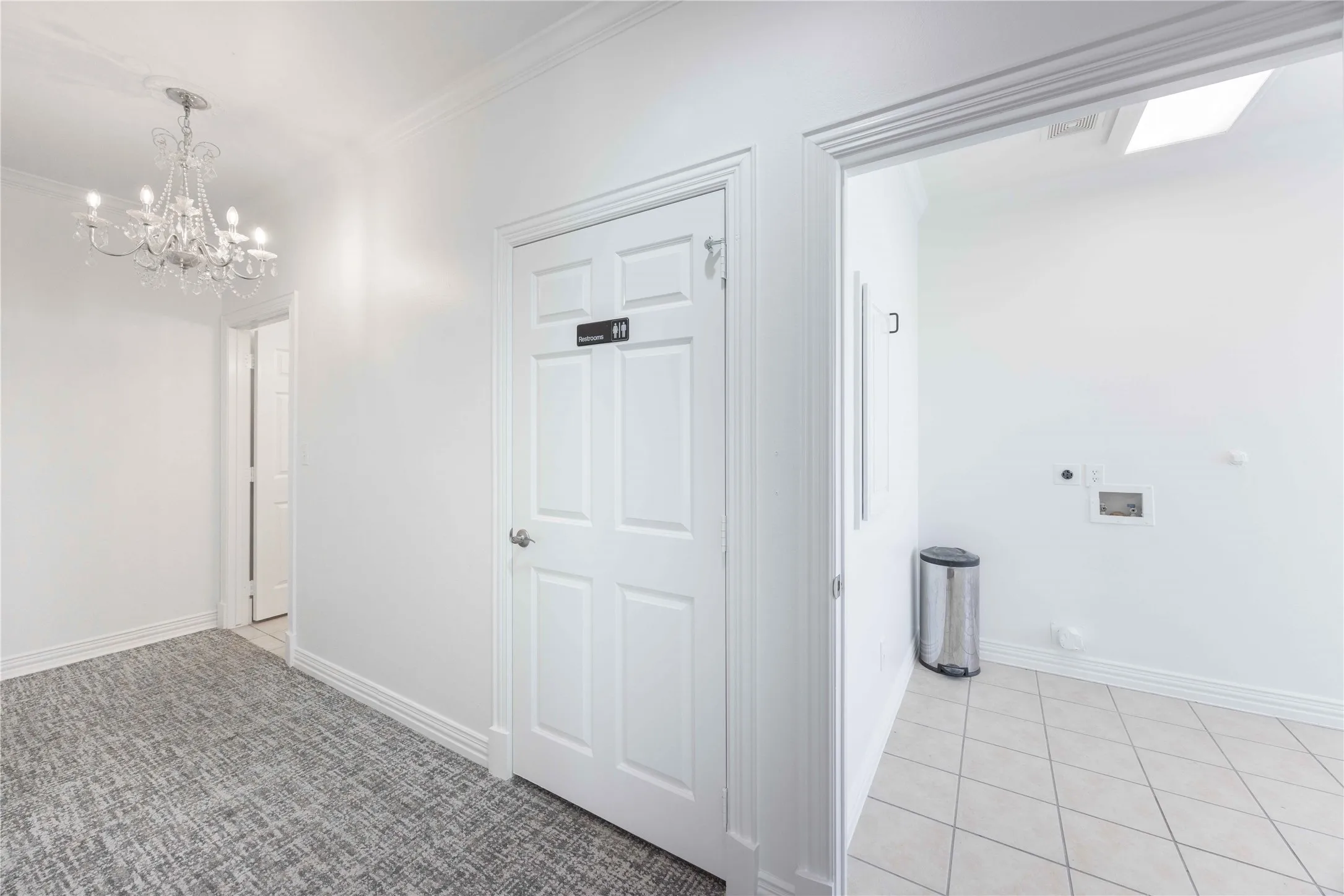 Chandelier lighting, crown molding, paneled interior door, tiled flooring, and a skylight