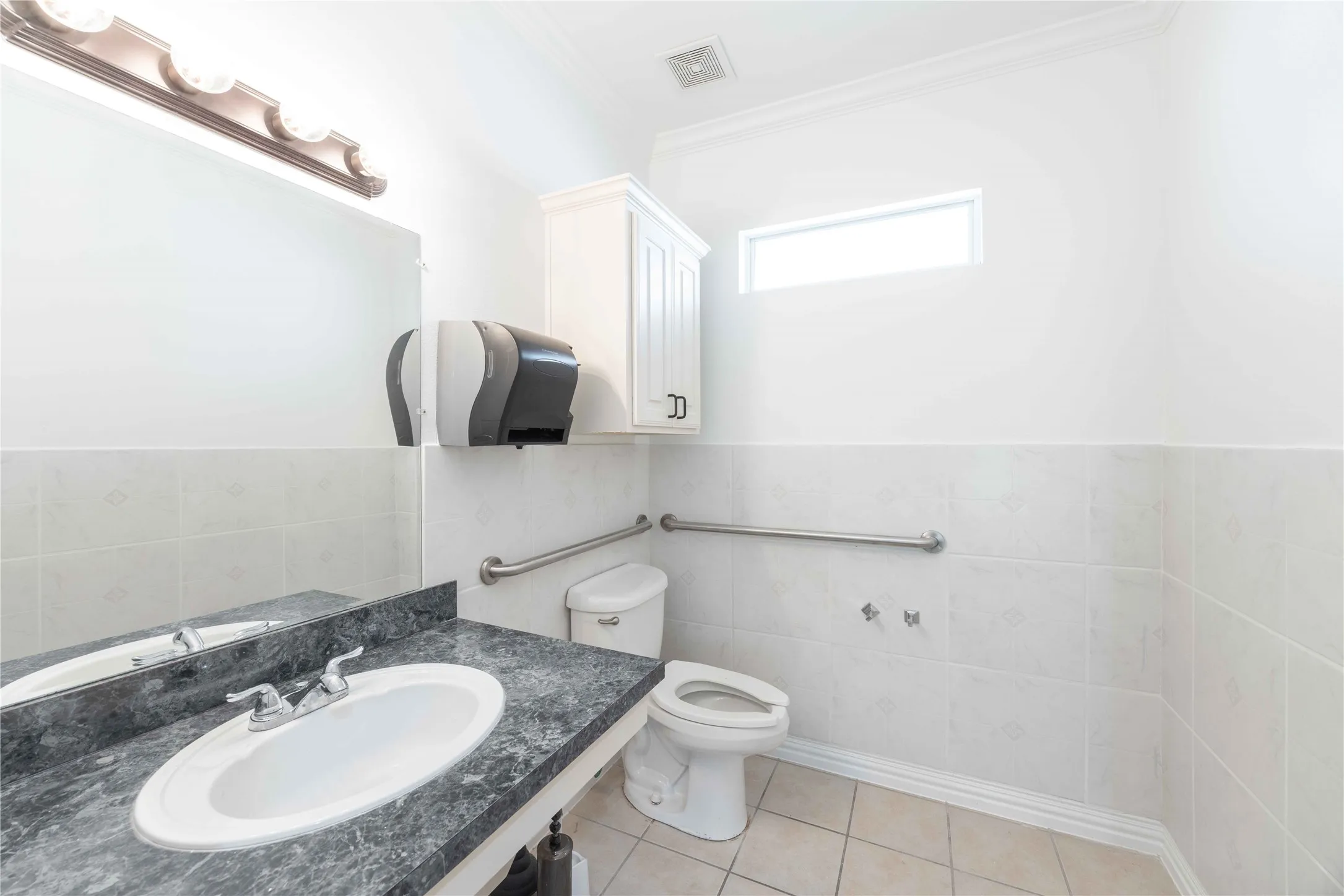 Vanity with an oval sink and a dark countertop, white wall-mounted cabinetry, white tiled walls, and a small rectangular window