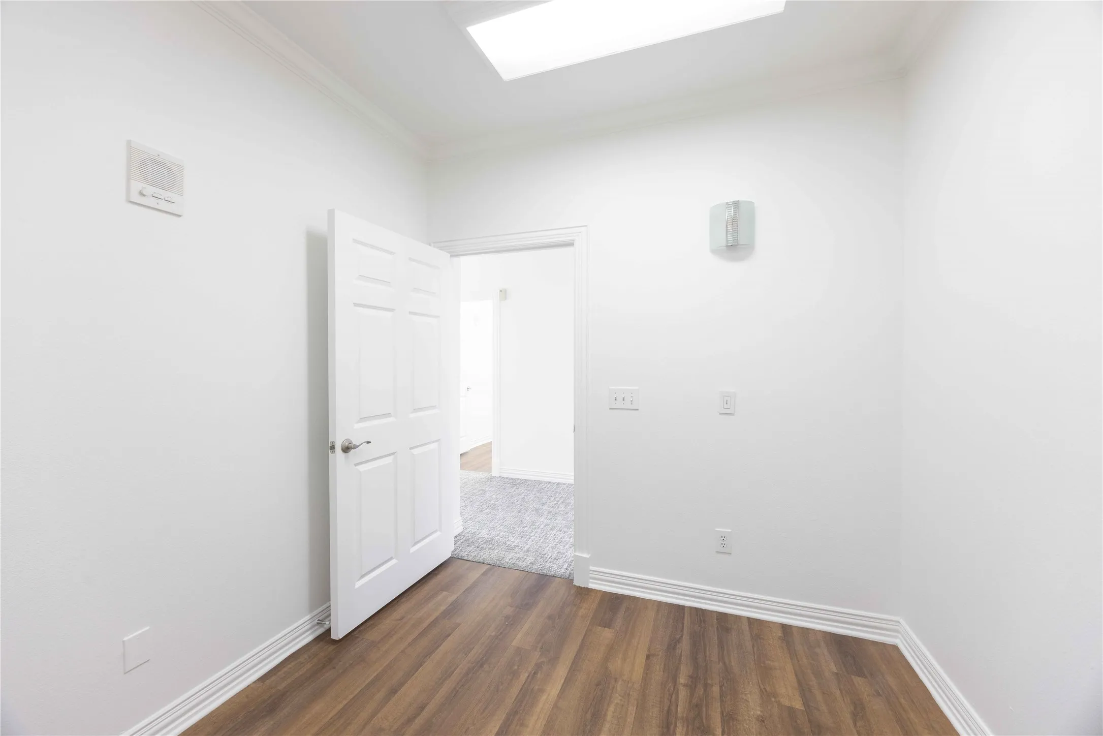 Wood-finish flooring, white paneled door, crown molding, and recessed lighting