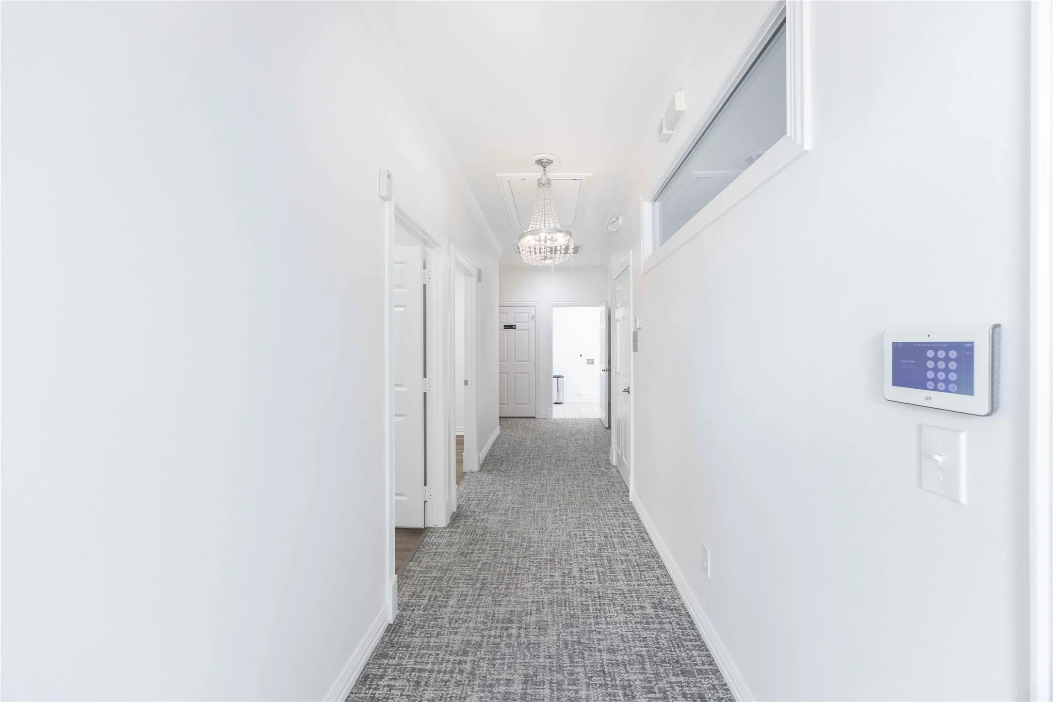 Hallway featuring white walls, patterned carpet, transom window, and a modern chandelier