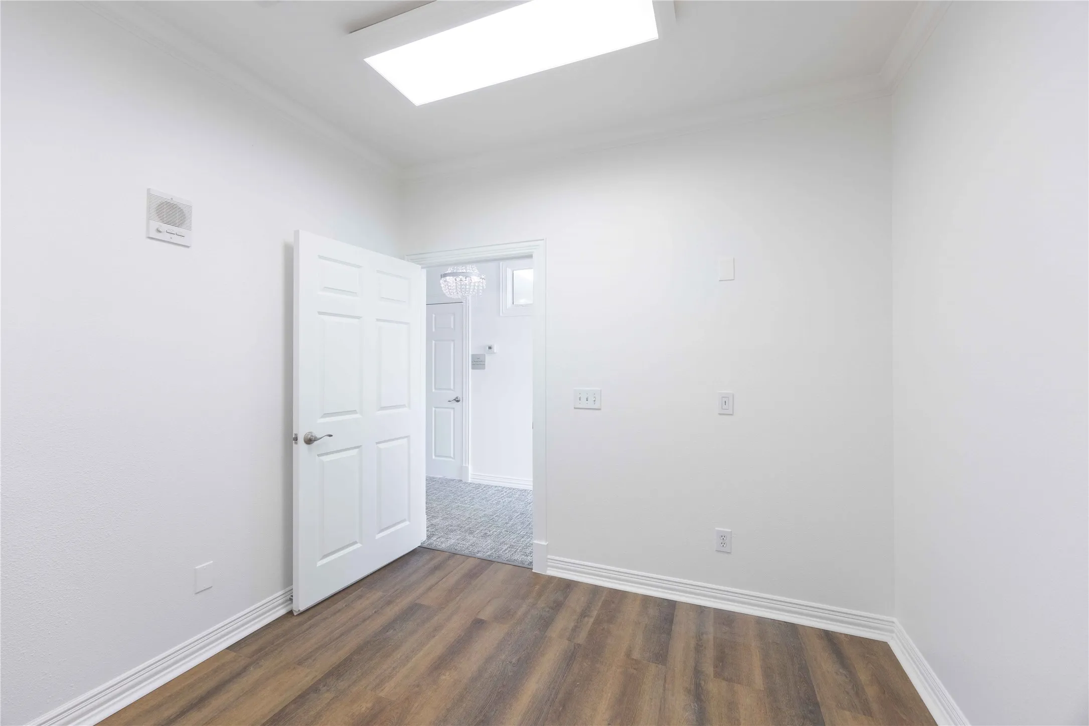 Wood-finish flooring, white paneled door, flush-mount lighting, and crown molding
