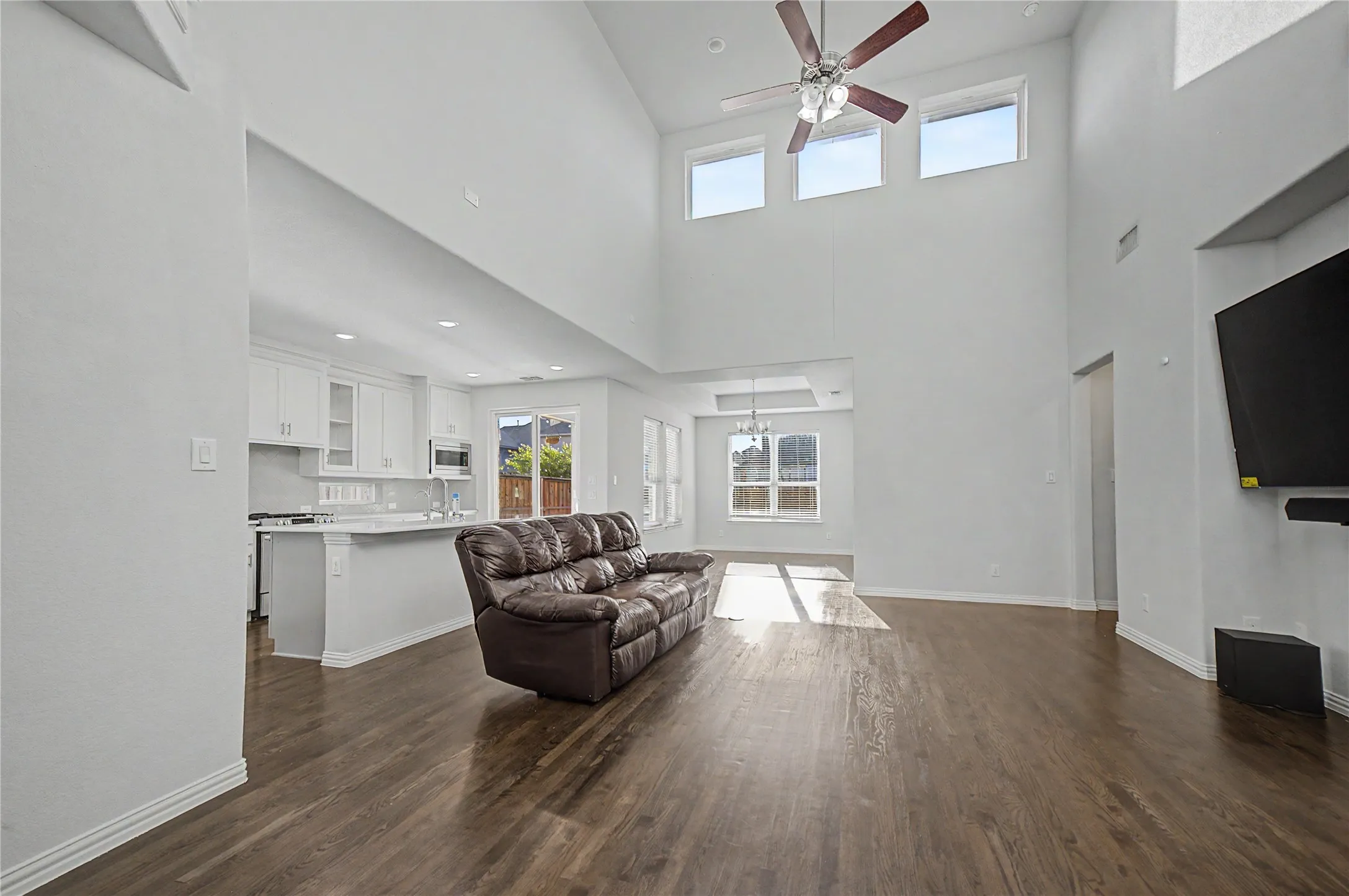 Vaulted ceiling, wood-finish flooring, recessed lighting, ceiling fan, and white cabinetry