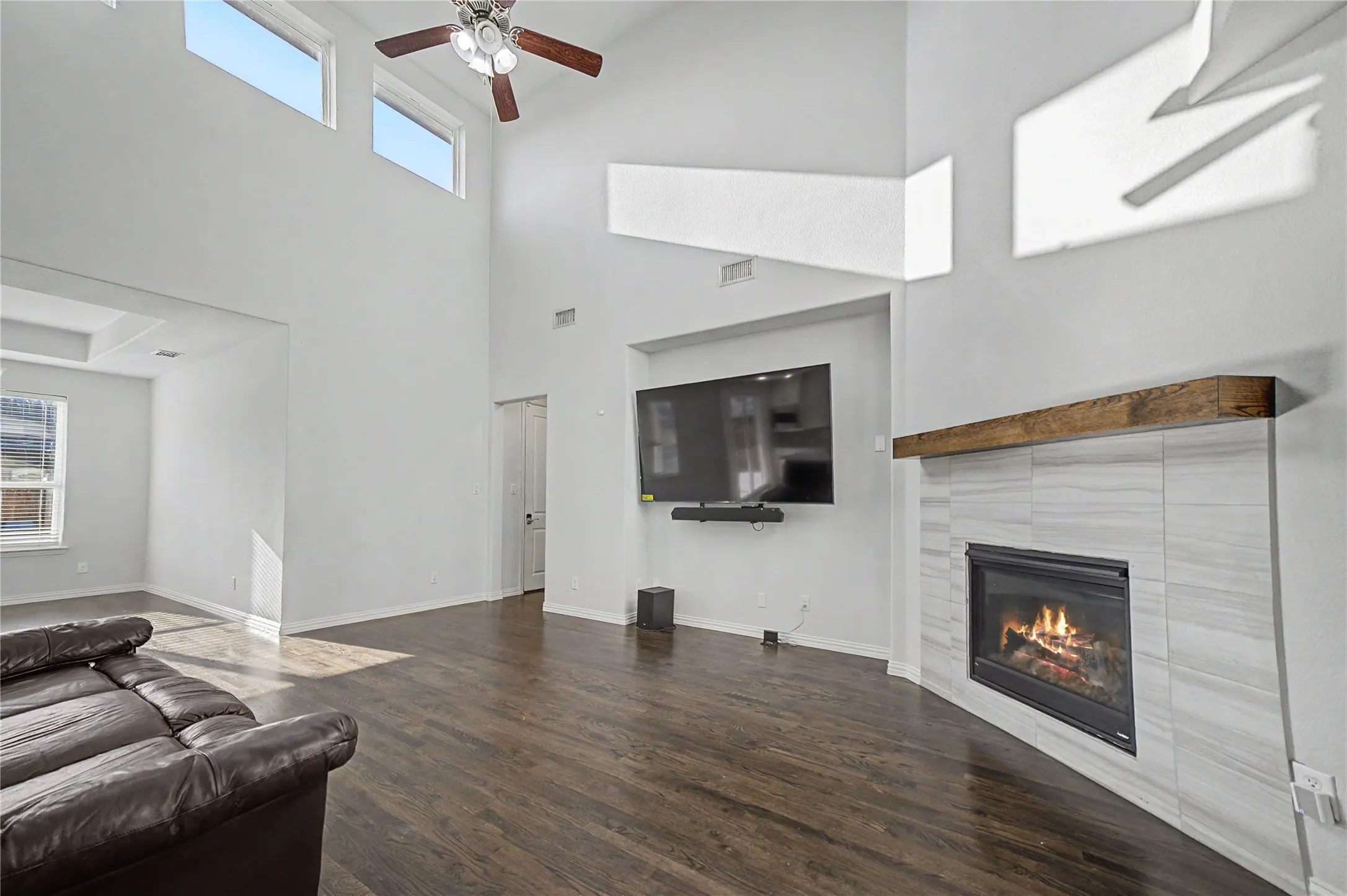 Vaulted ceilings with clerestory windows, wood-finish flooring, a ceiling fan, and a tiled fireplace with a wood mantle