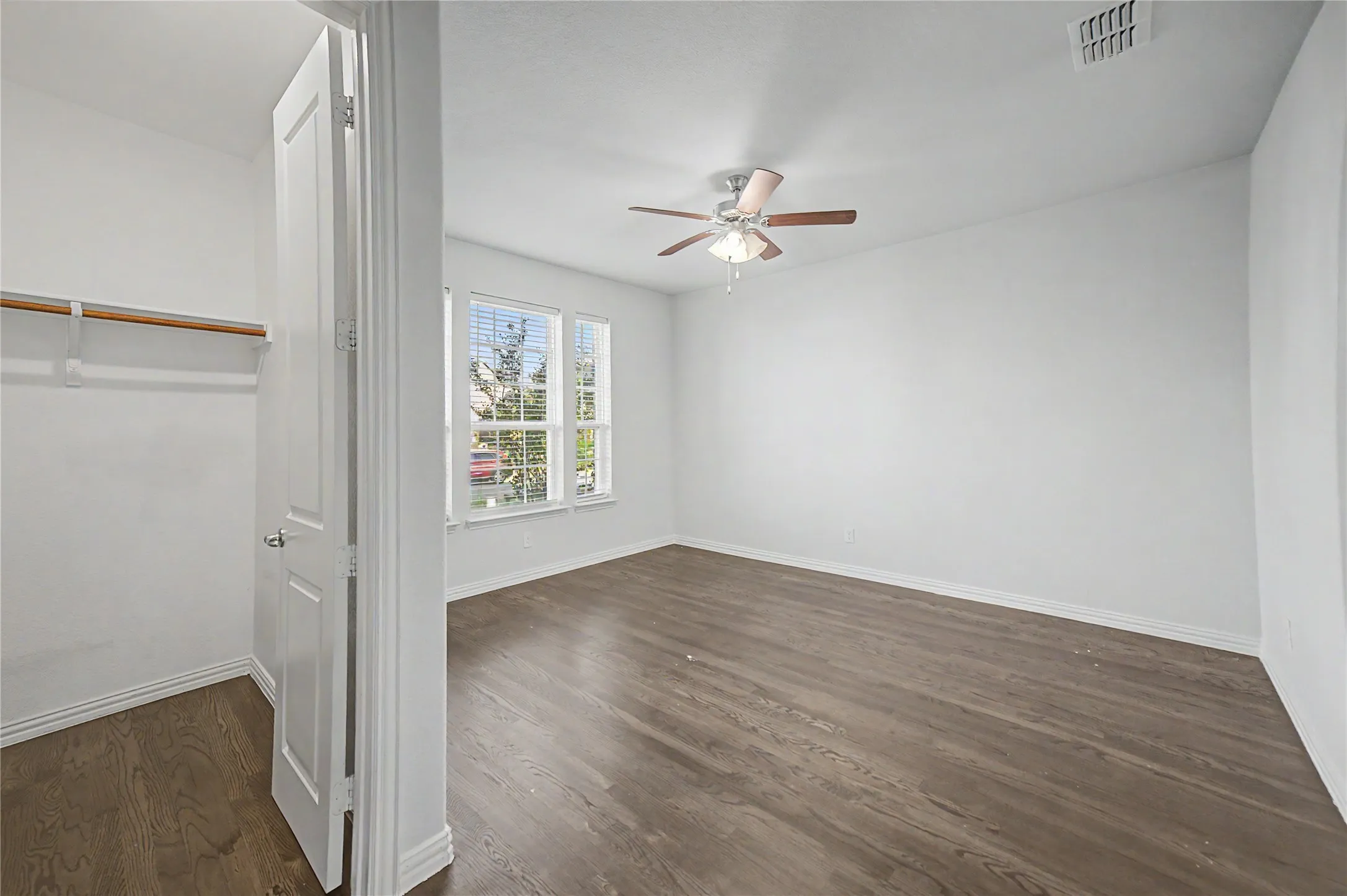 Spacious room featuring wood-finish flooring, multiple windows with blinds, a ceiling fan with integrated lighting, and a closet with a built-in hanging rod