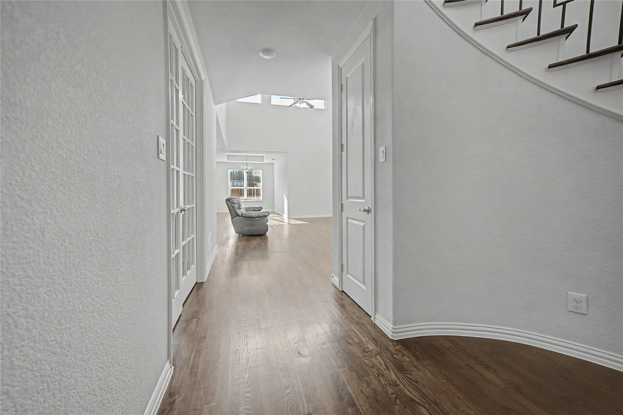 Wood-finish flooring throughout, white interior walls, and a modern staircase with dark risers and metal balusters