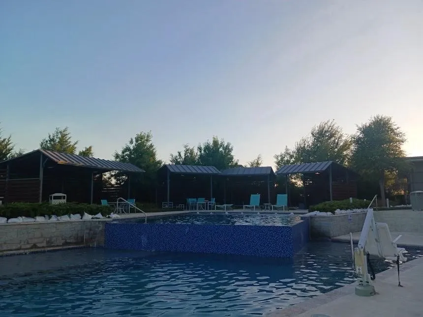 Swimming pool with mosaic tile detailing, multiple poolside cabanas, and a concrete deck