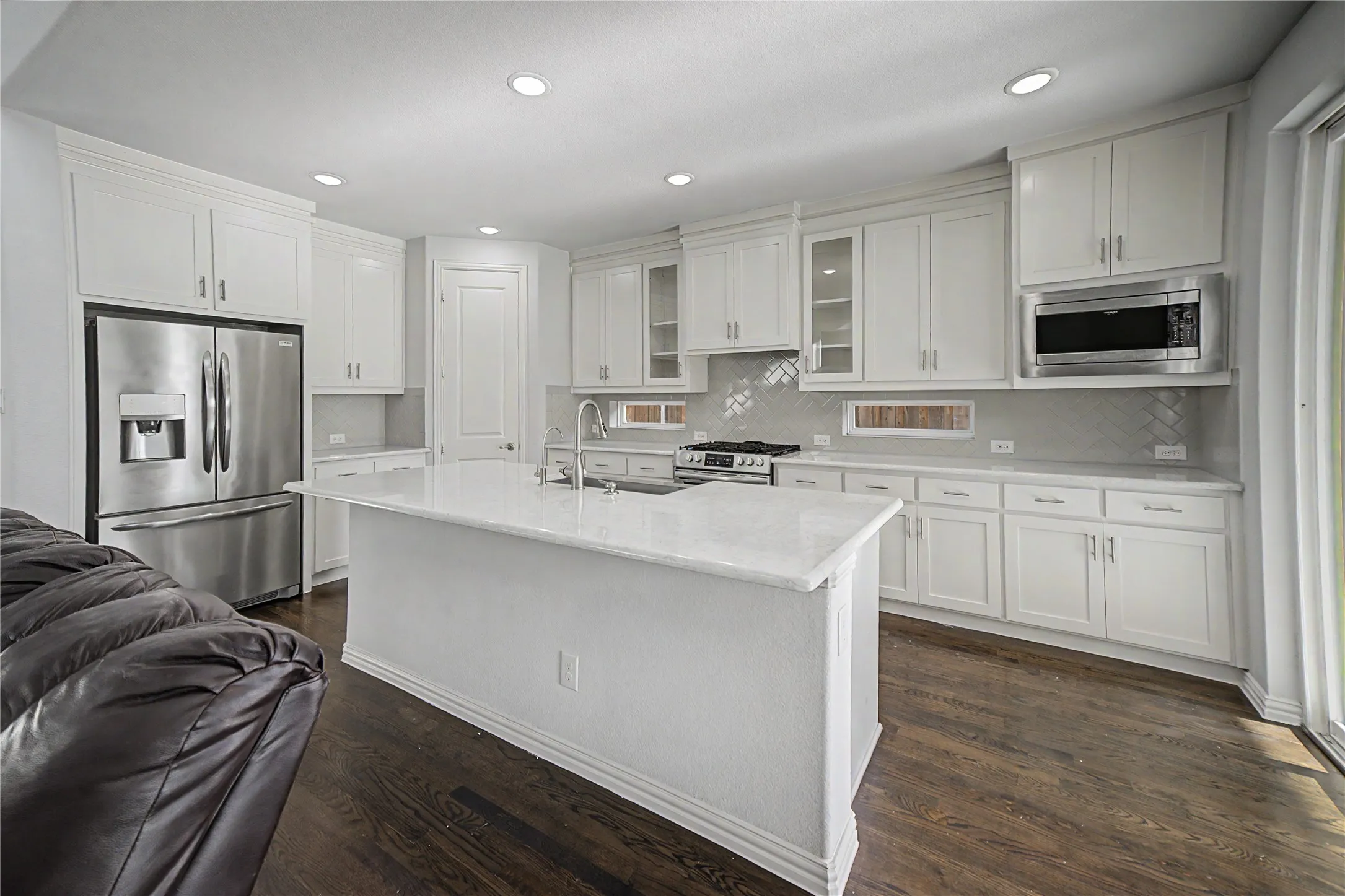 White cabinetry, stainless steel appliances, central island with sink, wood-finish flooring, recessed lighting